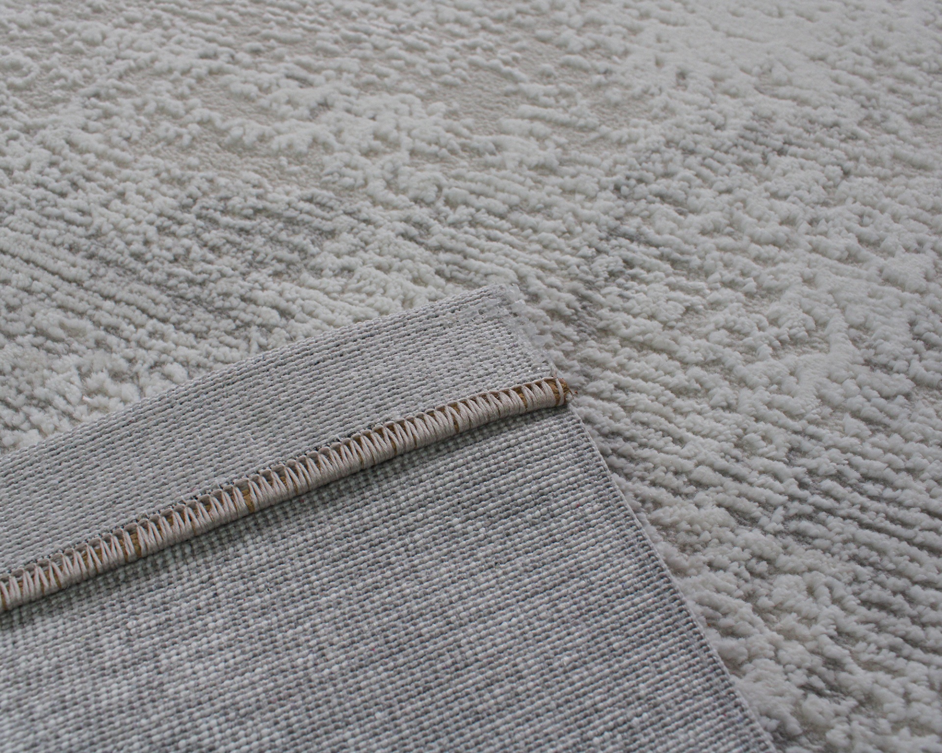 Pormenor de tapete cinzento claro com padrão texturizado e verso com costura