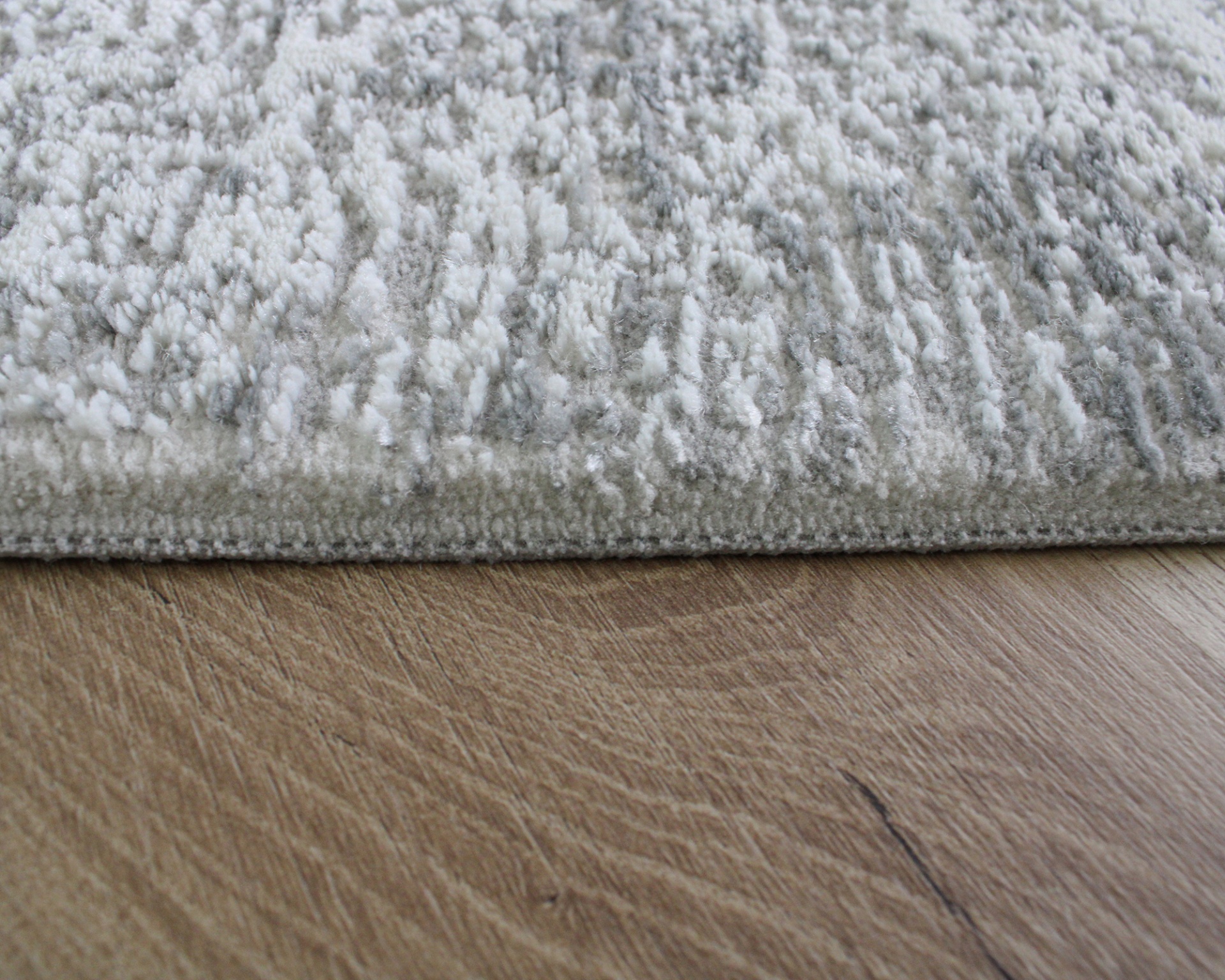Tapete cinza claro com textura felpuda sobre chão de madeira clara