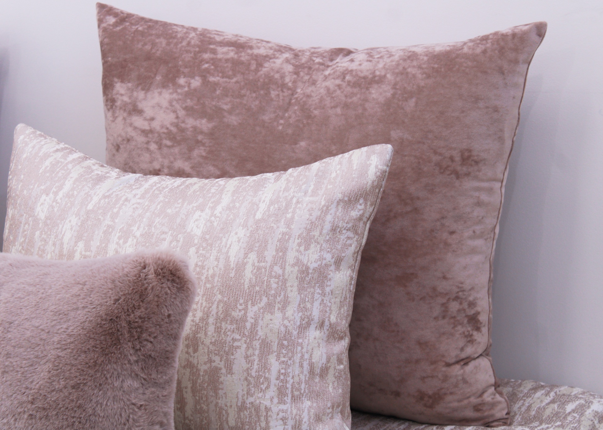 Três almofadas decorativas em tons neutros com diferentes texturas e padrões