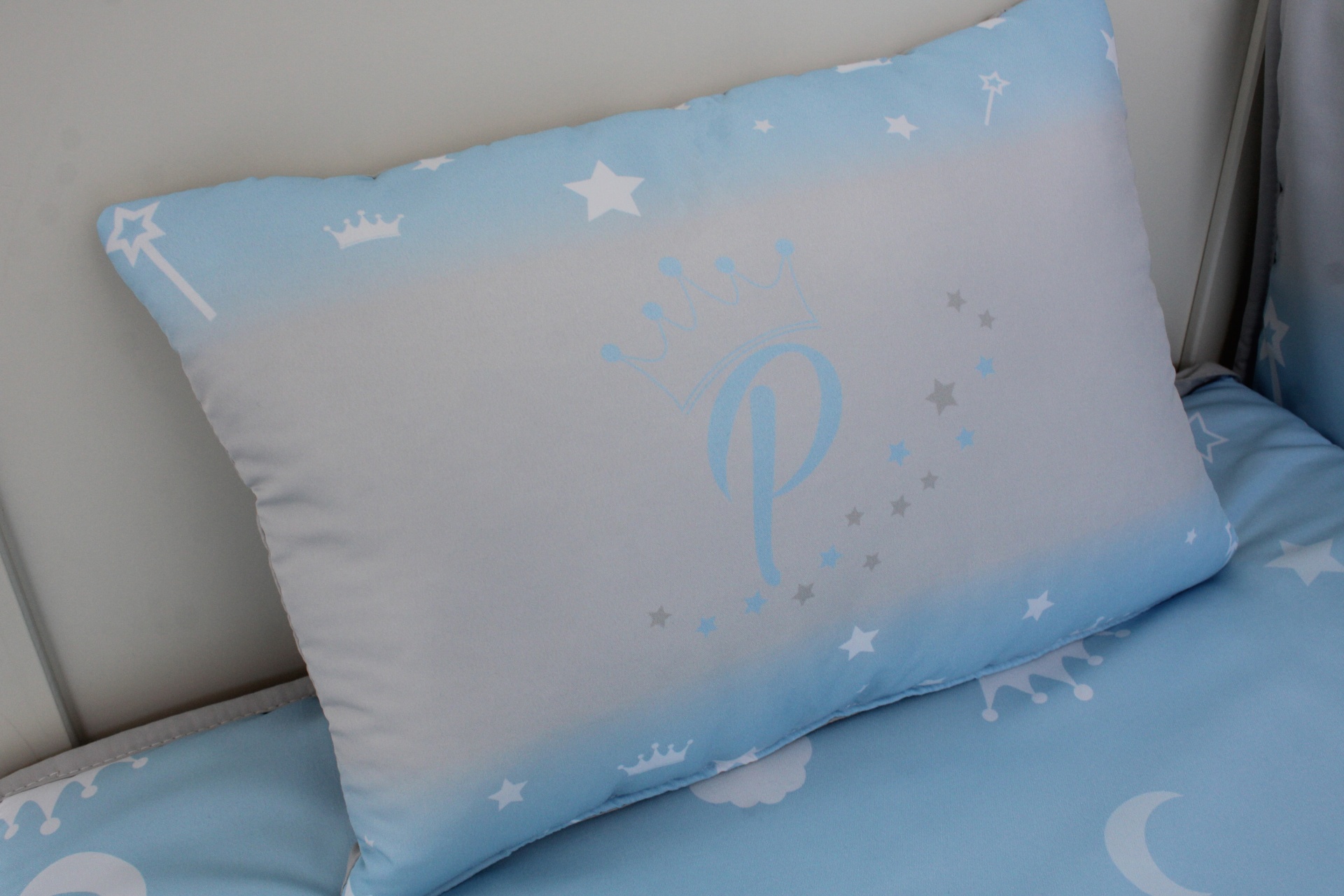 Almofada azul com padrão de estrelas, coroas e a letra P ao centro