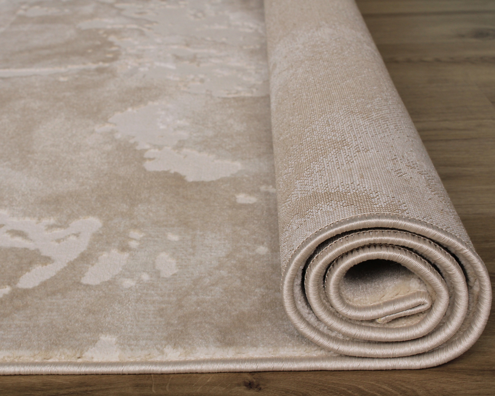 Tapete bege enrolado parcialmente com padrão abstrato sobre chão de madeira