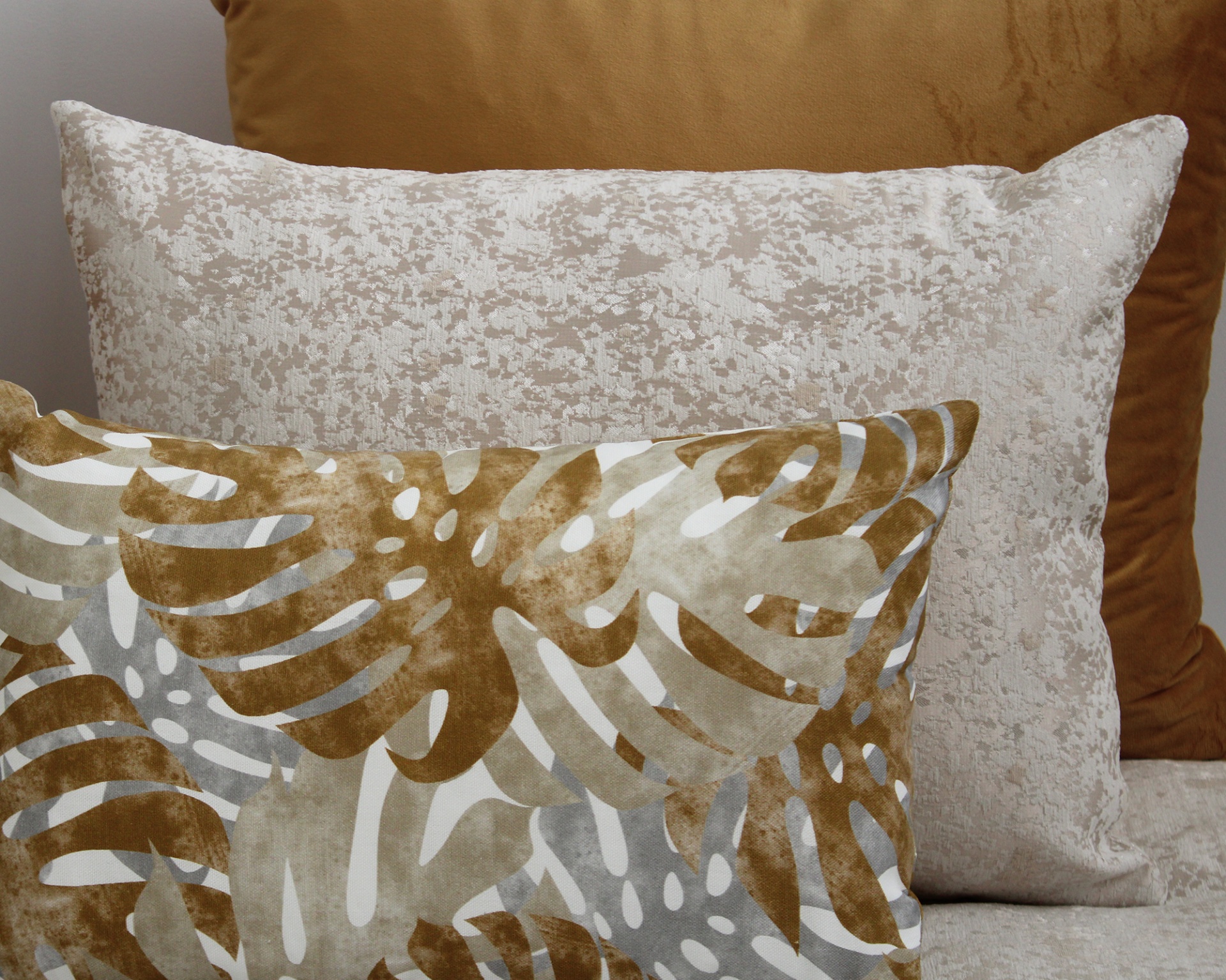 Três almofadas decorativas em diferentes padrões e texturas sobre sofá cinza claro.