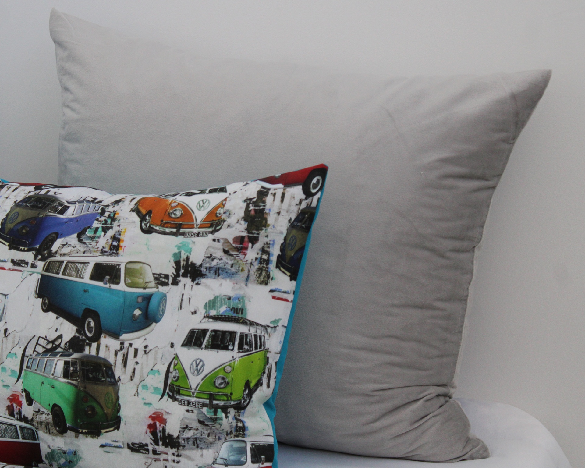 Duas almofadas, uma cinza lisa e outra com estampa colorida de carrinhas Volkswagen