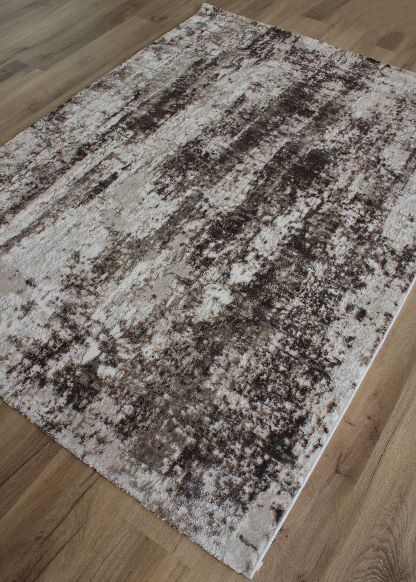 Tapete com padrão abstrato em tons de bege, marrom e cinza sobre pavimento de madeira clara