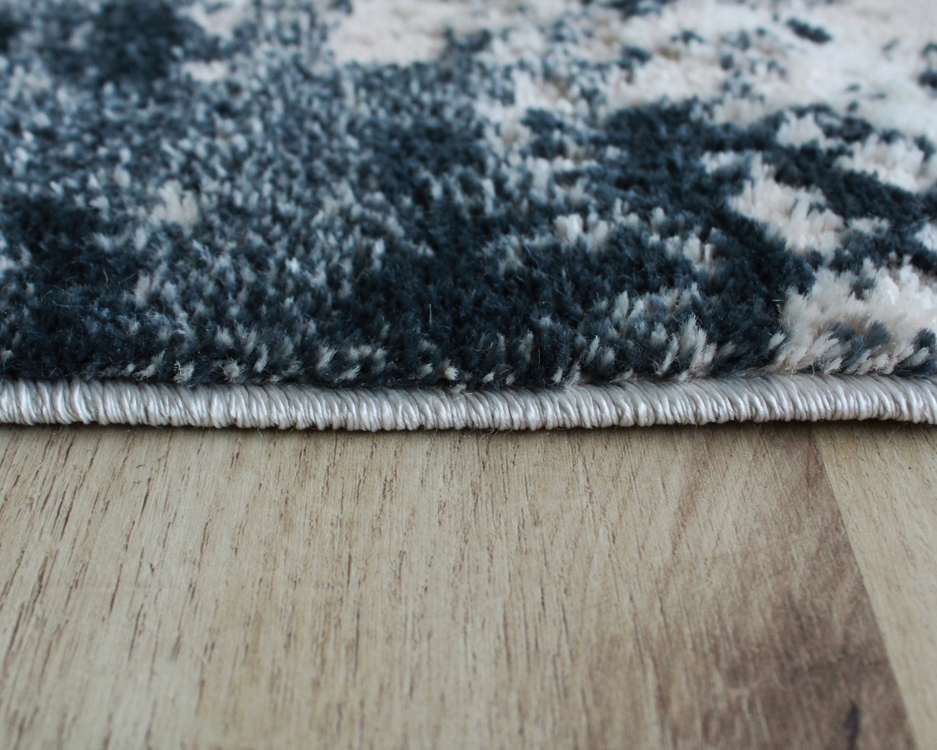 Tapete cinza e branco com borda em ponto branco sobre chão madeira clara