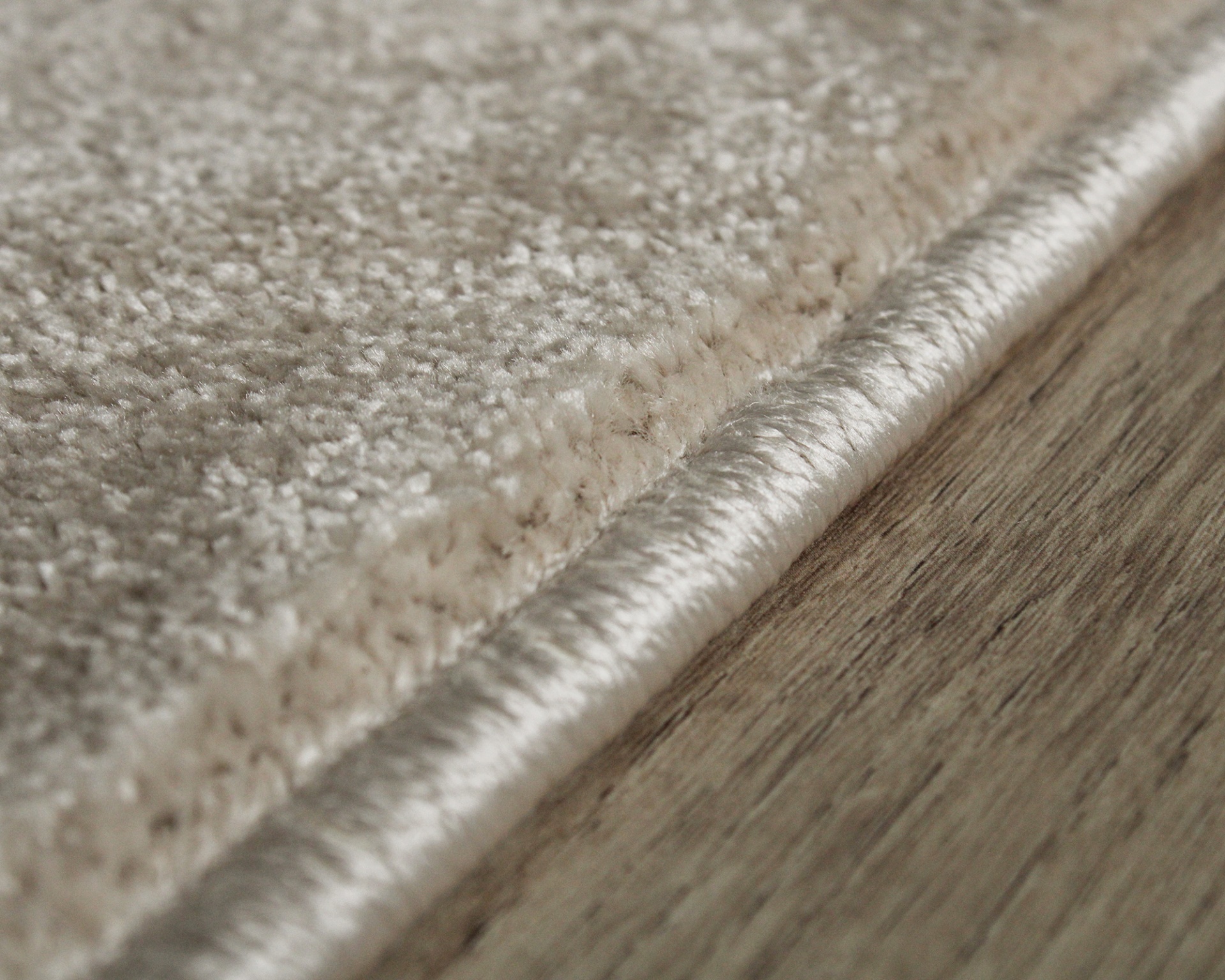 Tapete bege claro com textura aveludada e bordas de fio brilhante sobre chão de madeira clara