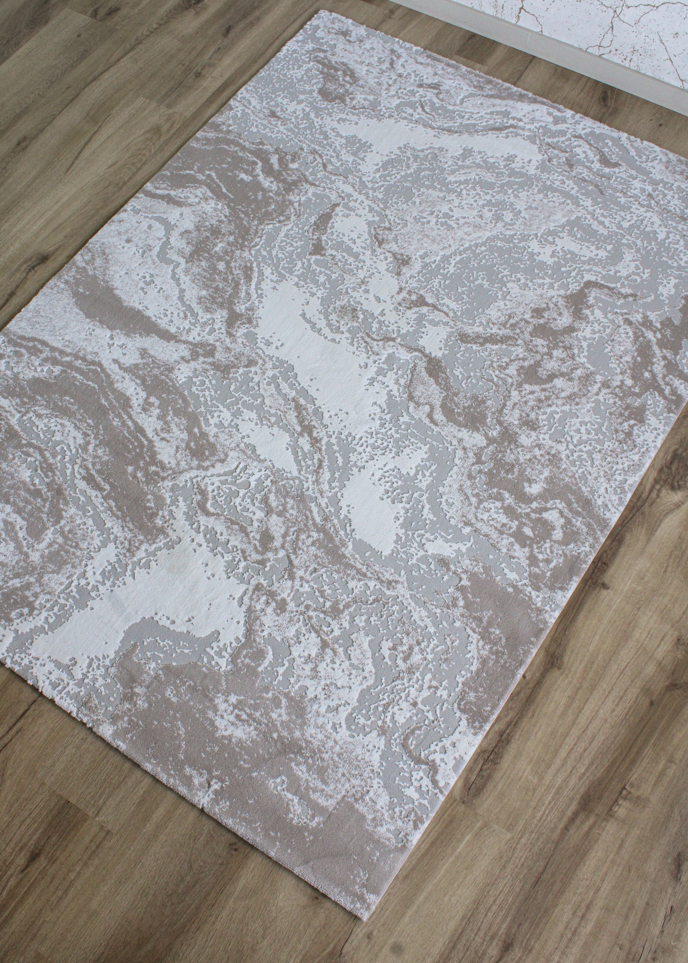 Tapete cinza e bege com padrão abstrato sobre chão de madeira clara