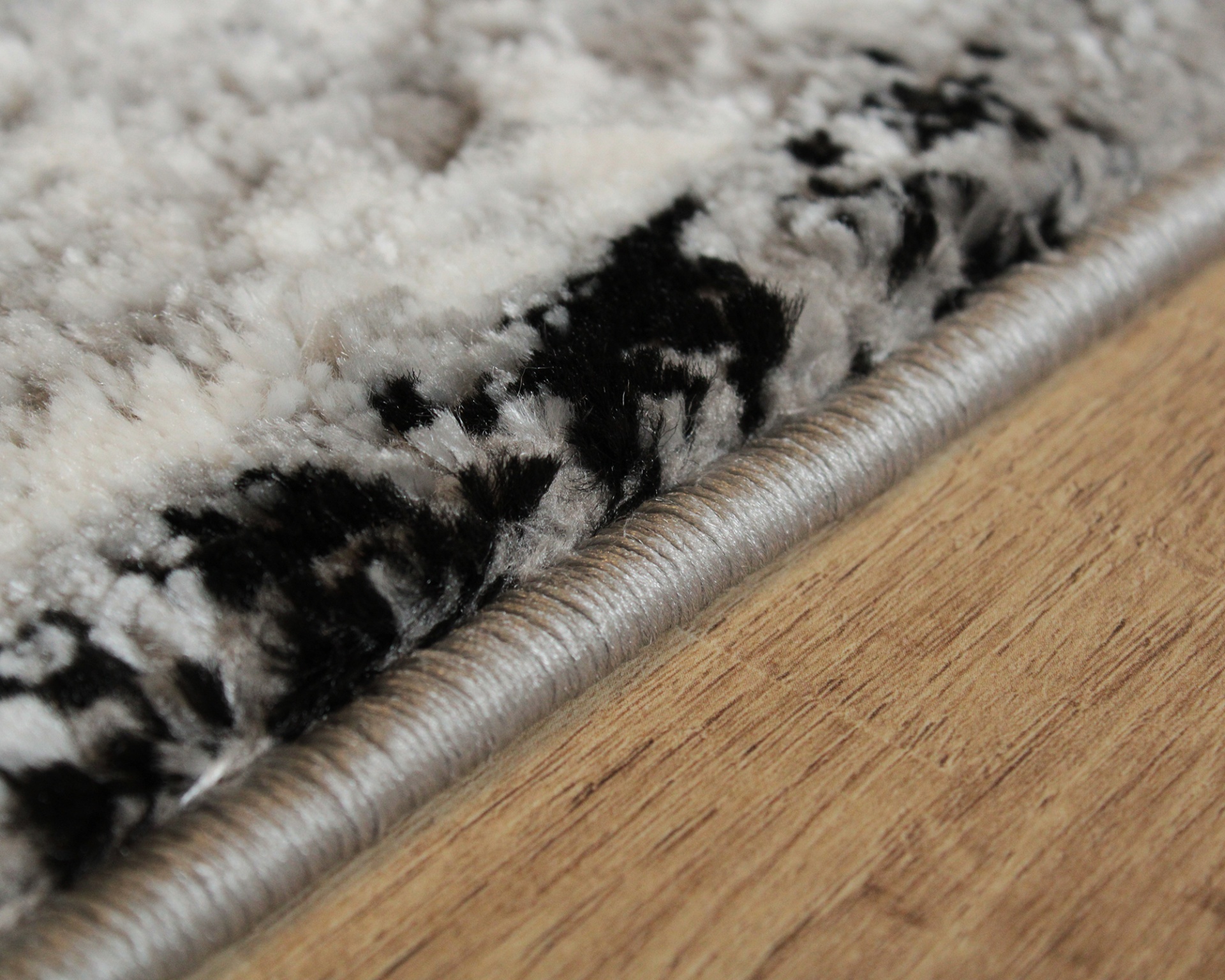 Tapete felpudo preto e branco com borda cinza sobre chão de madeira clara