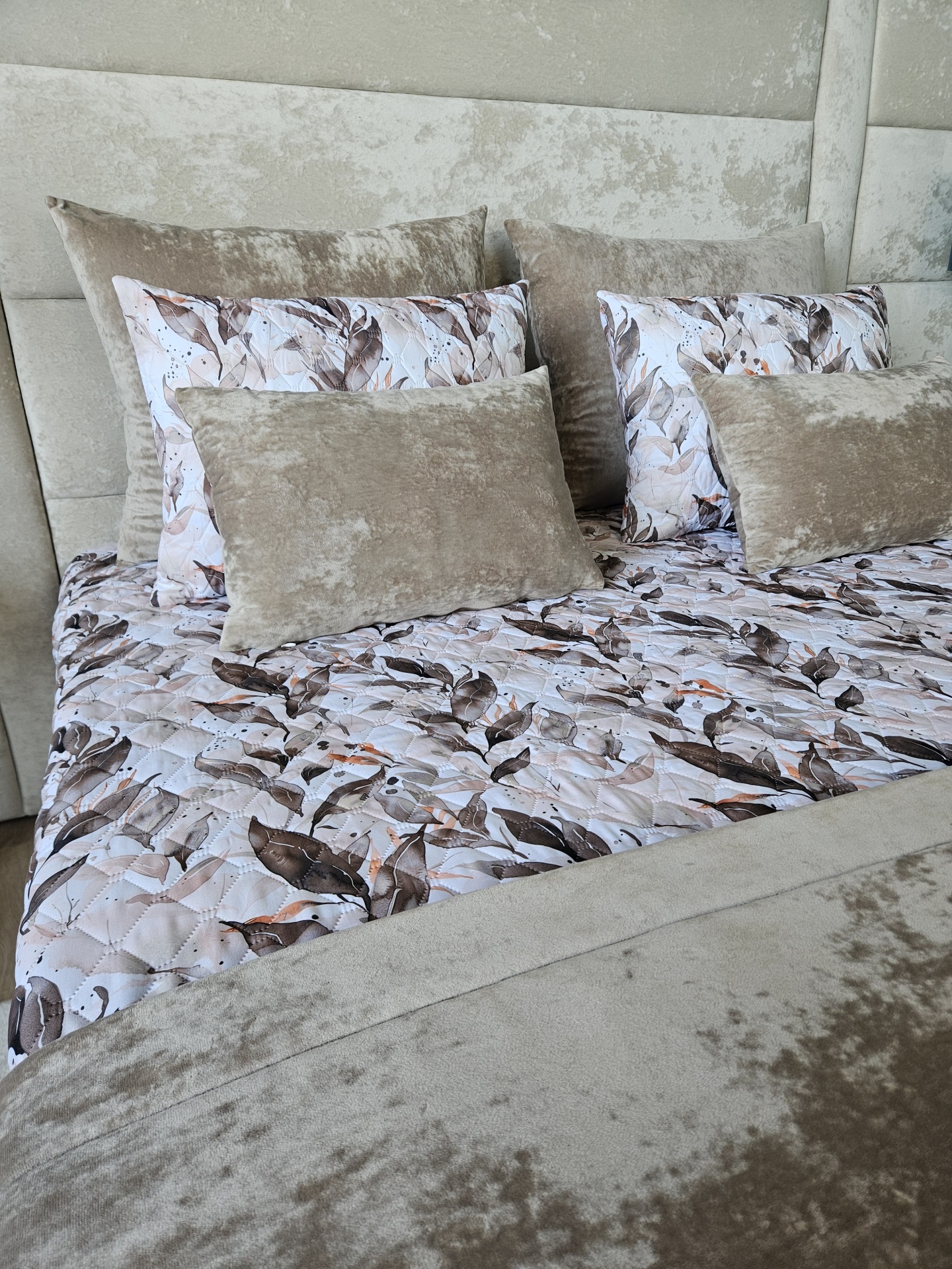 Cama com roupa de cama em padrão de folhas castanhas e almofadas bege aveludadas
