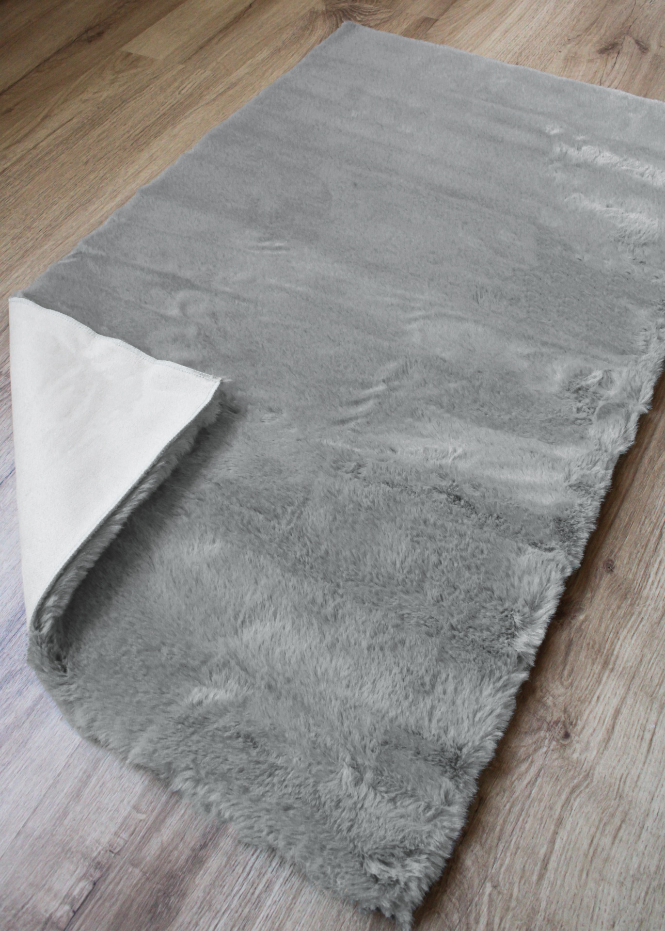 Tapete cinzento peludo com canto dobrado, sobre chão de madeira clara
