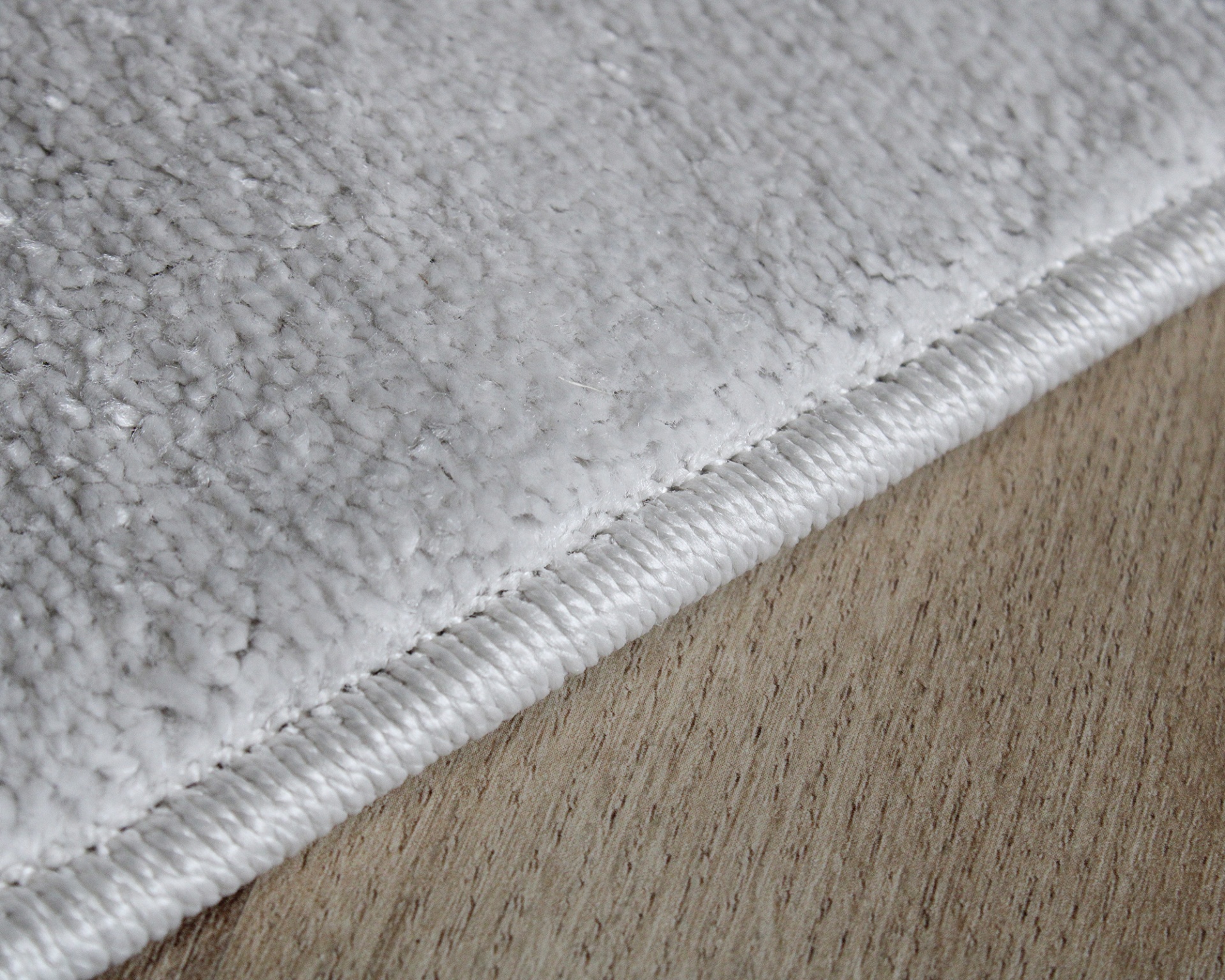 Tapete cinza claro com textura aveludada e borda branca sobre pavimento de madeira