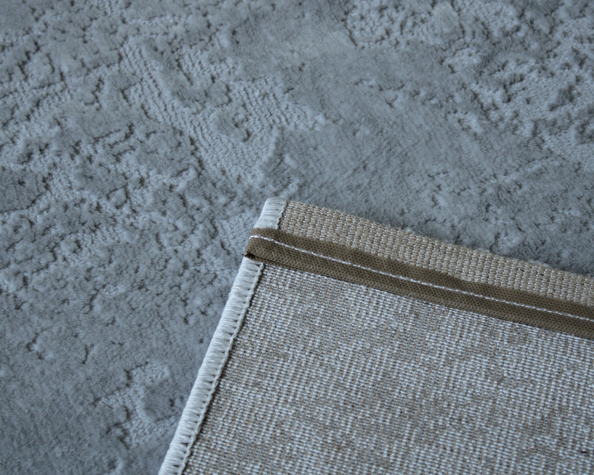 Canto de tapete bege com bordado branco sobre piso cinza texturado
