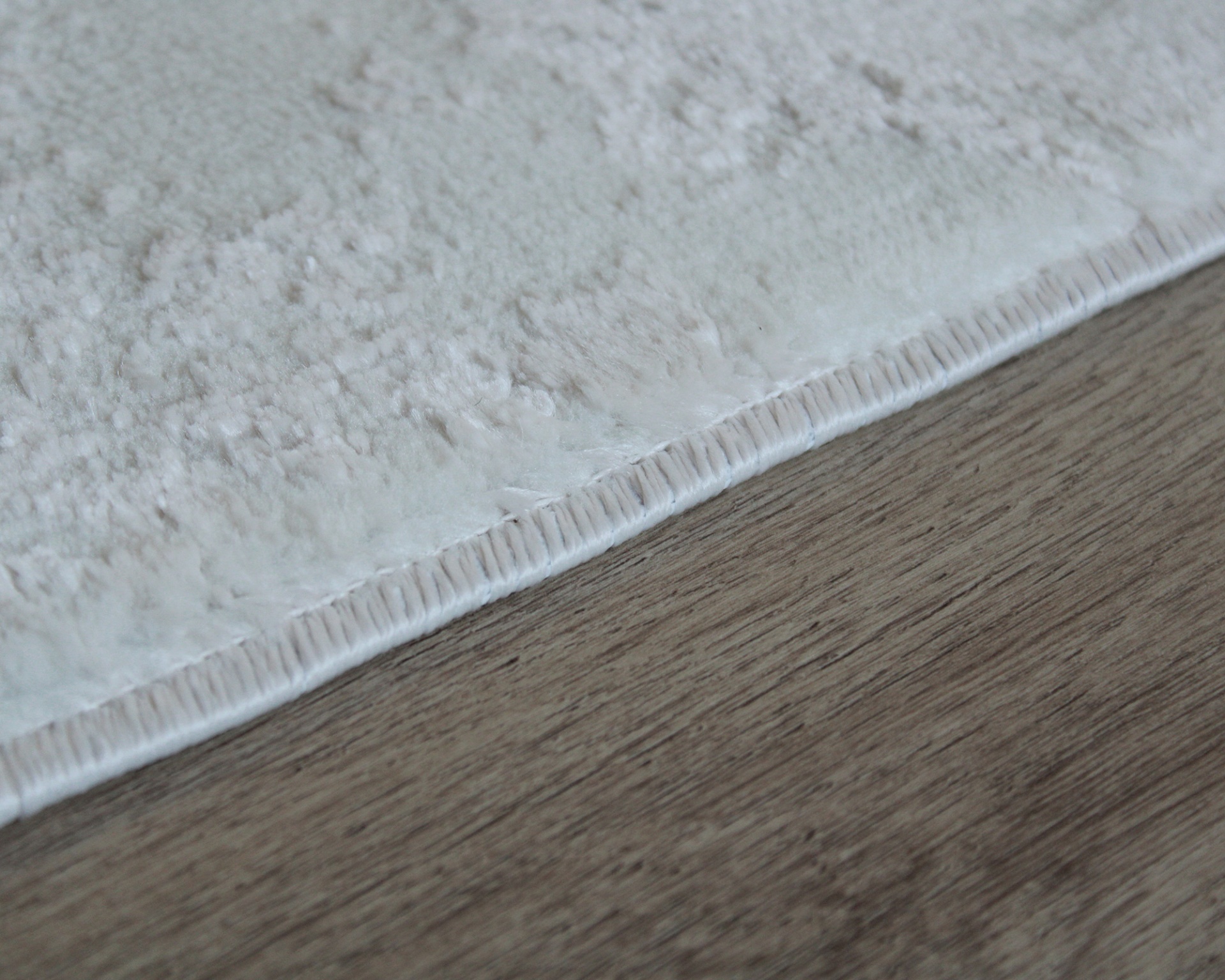 Tapete cinza claro com bordas costuradas sobre chão de madeira