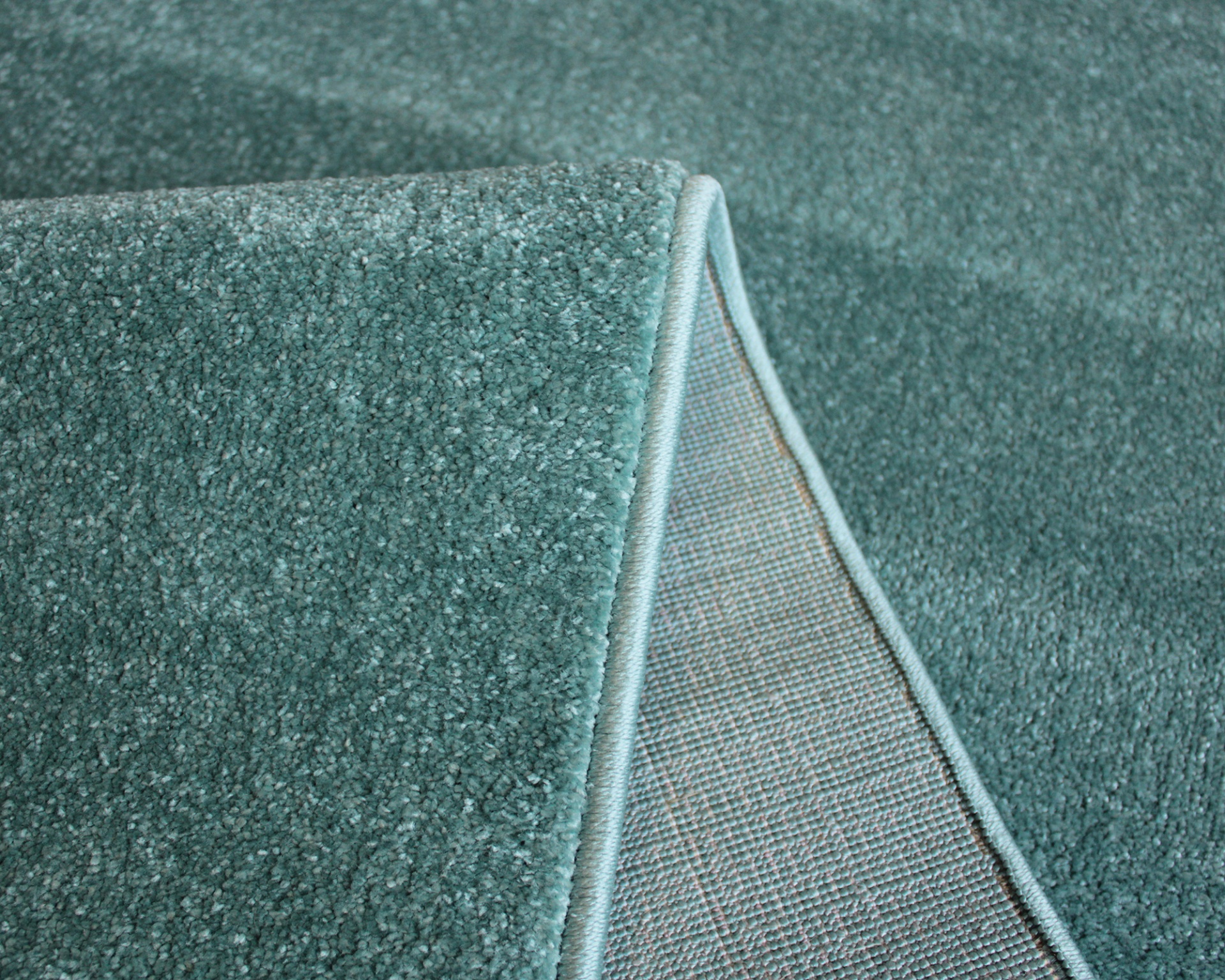 Tapete azul-petróleo com textura felpuda e detalhe da dobra mostrando o avesso.