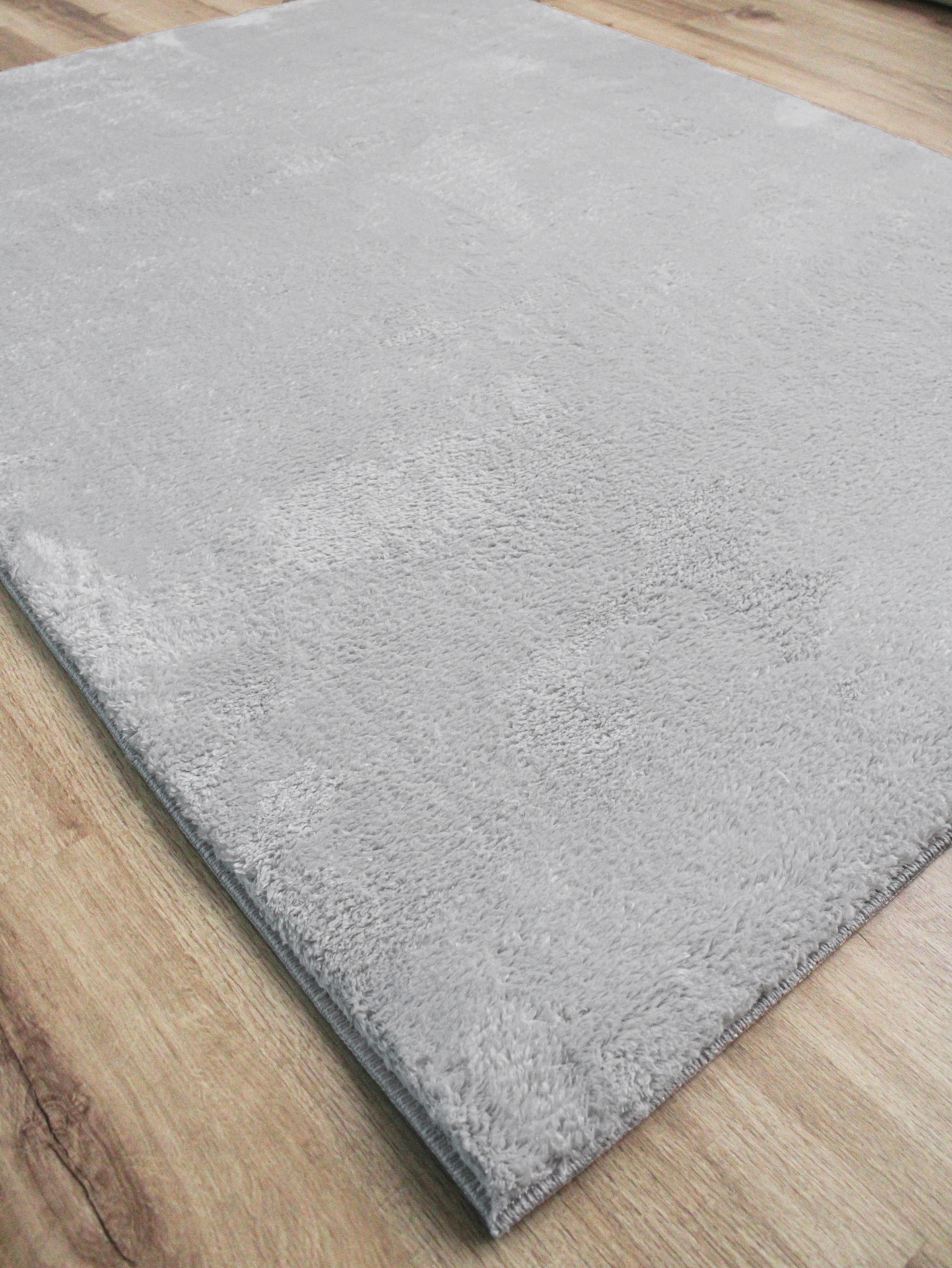Tapete cinzento claro felpudo sobre chão de madeira clara