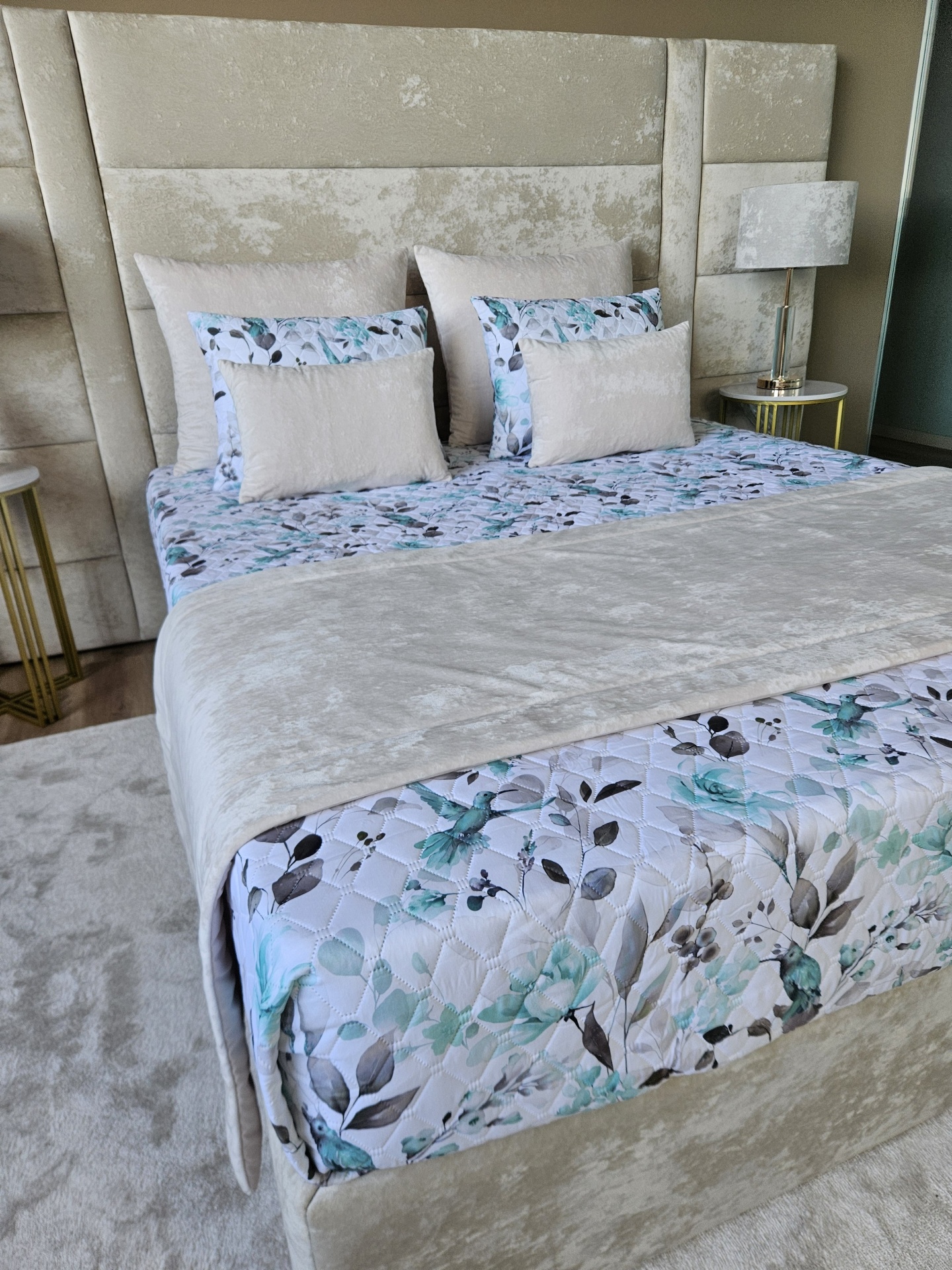 Cama estofada creme com roupa de cama floral e almofadas creme