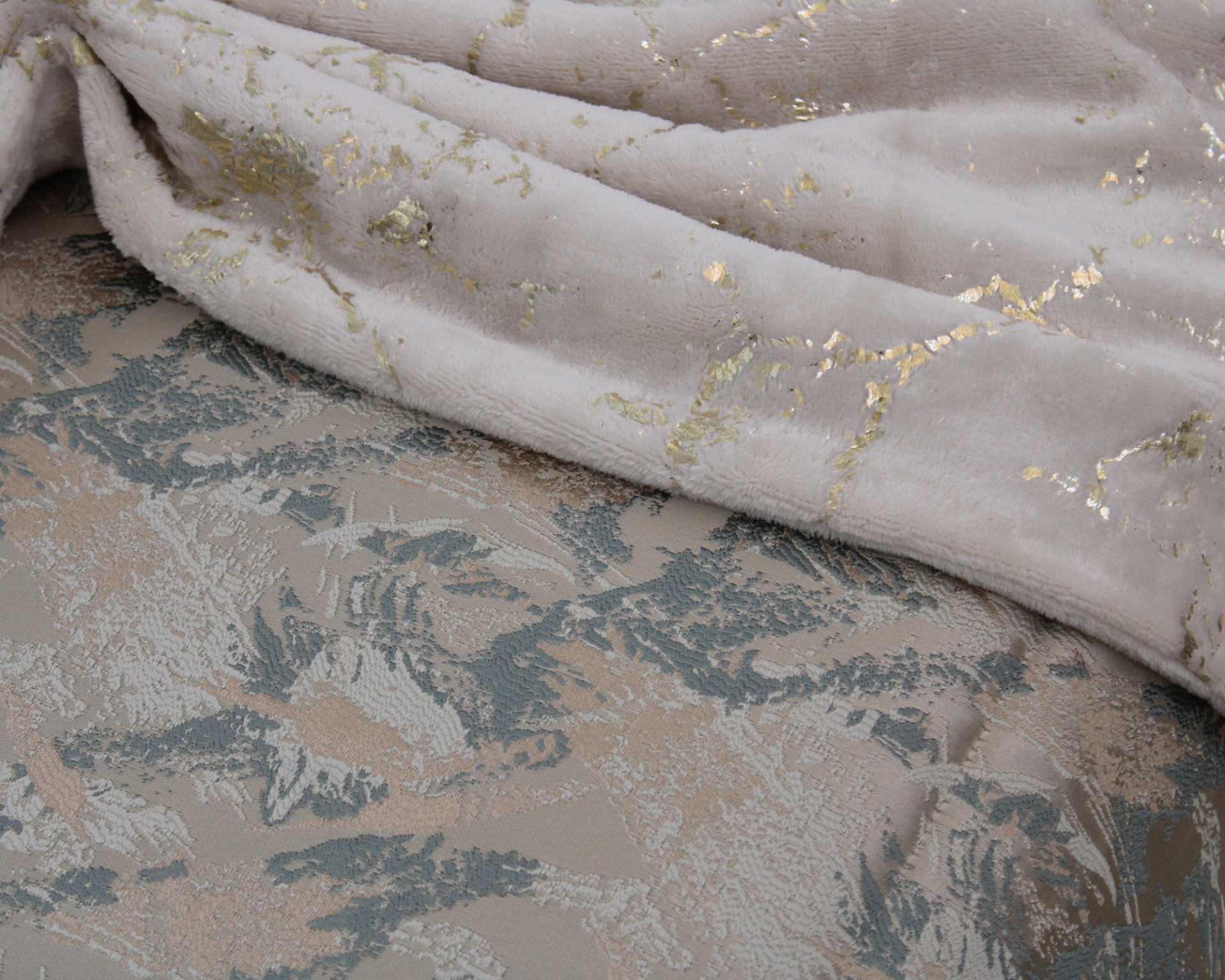 Cobertor cinza claro com detalhes dourados sobre manta floral bege e cinza