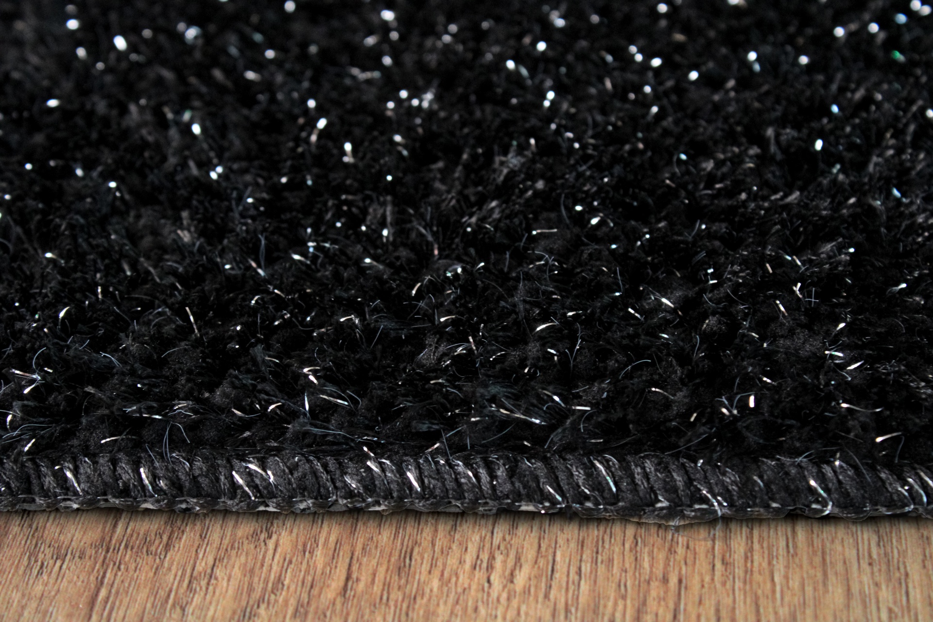 Tapete preto felpudo com borda costurada sobre chão de madeira