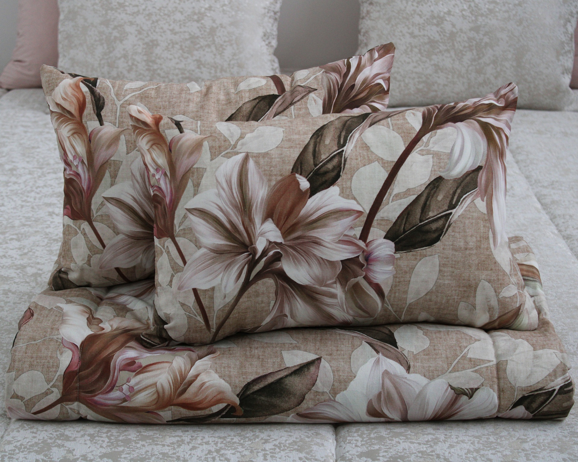 Almofadas e edredão florais em tons castanhos e bege sobre cama clara