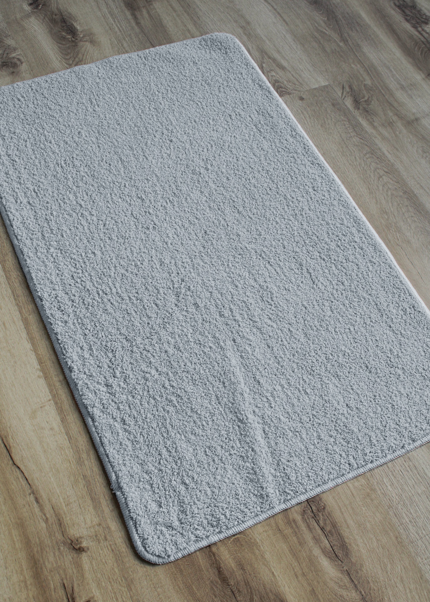 Tapete cinzento claro retangular com textura sobre chão de madeira