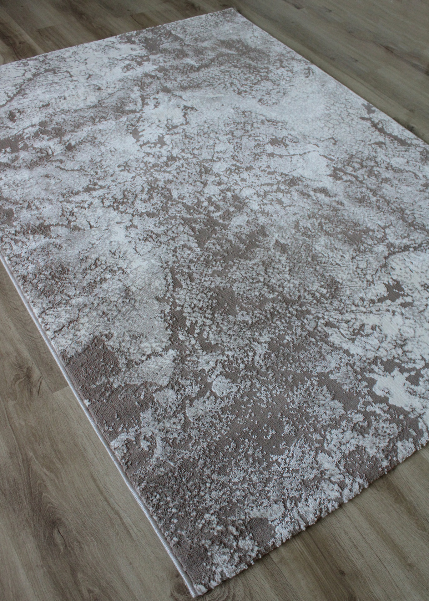 Tapete rectangular cinza claro e bege com padrão texturizado sobre chão de madeira