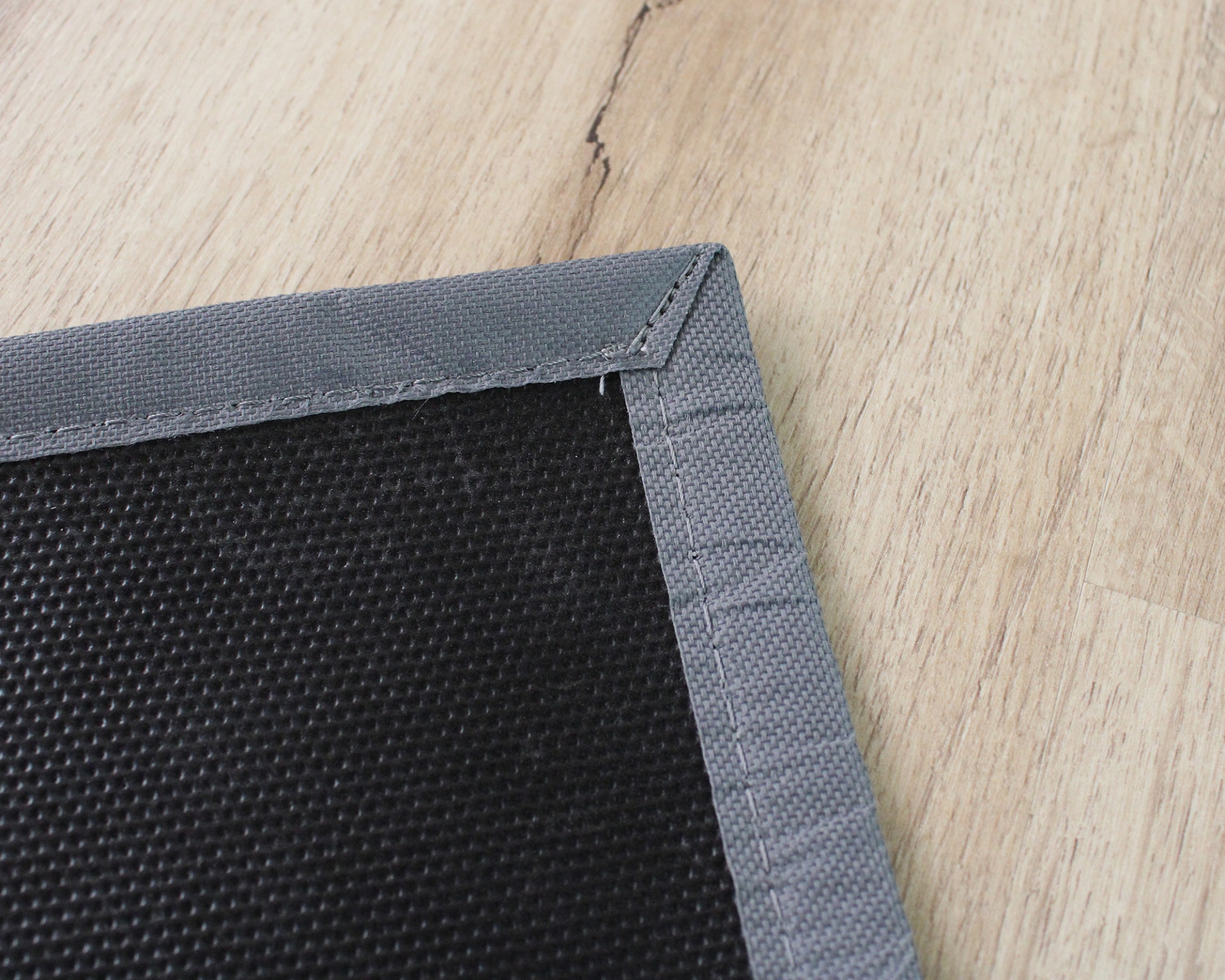 Tecido preto com bordas cinzentas sobre chão de madeira clara