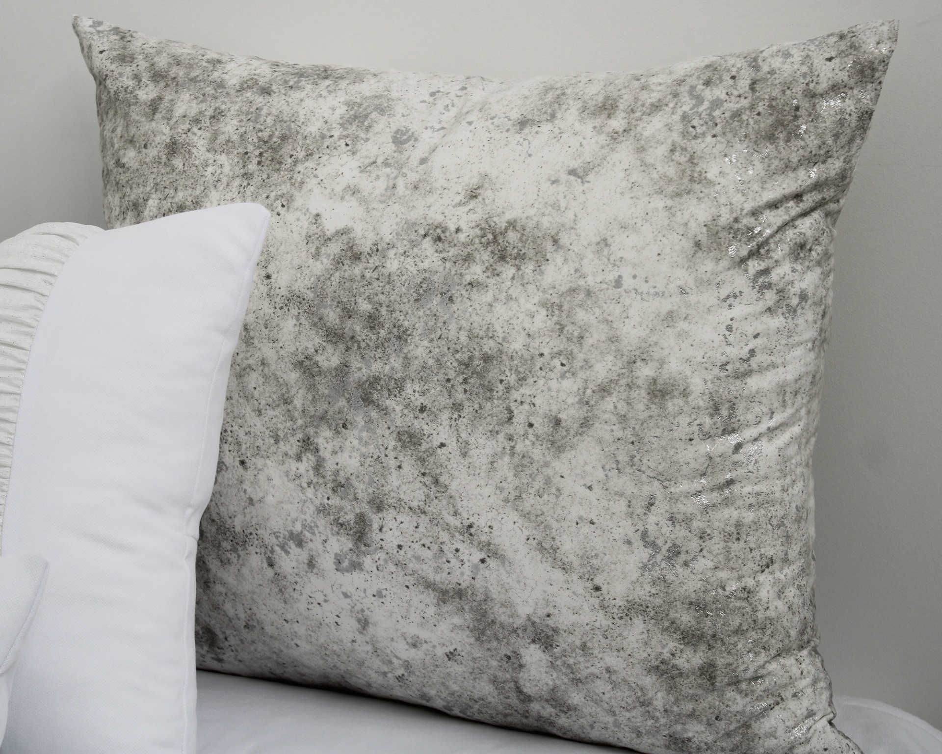 Almofada quadrada cinza claro com manchas cinzentas escuras ao lado de almofada branca