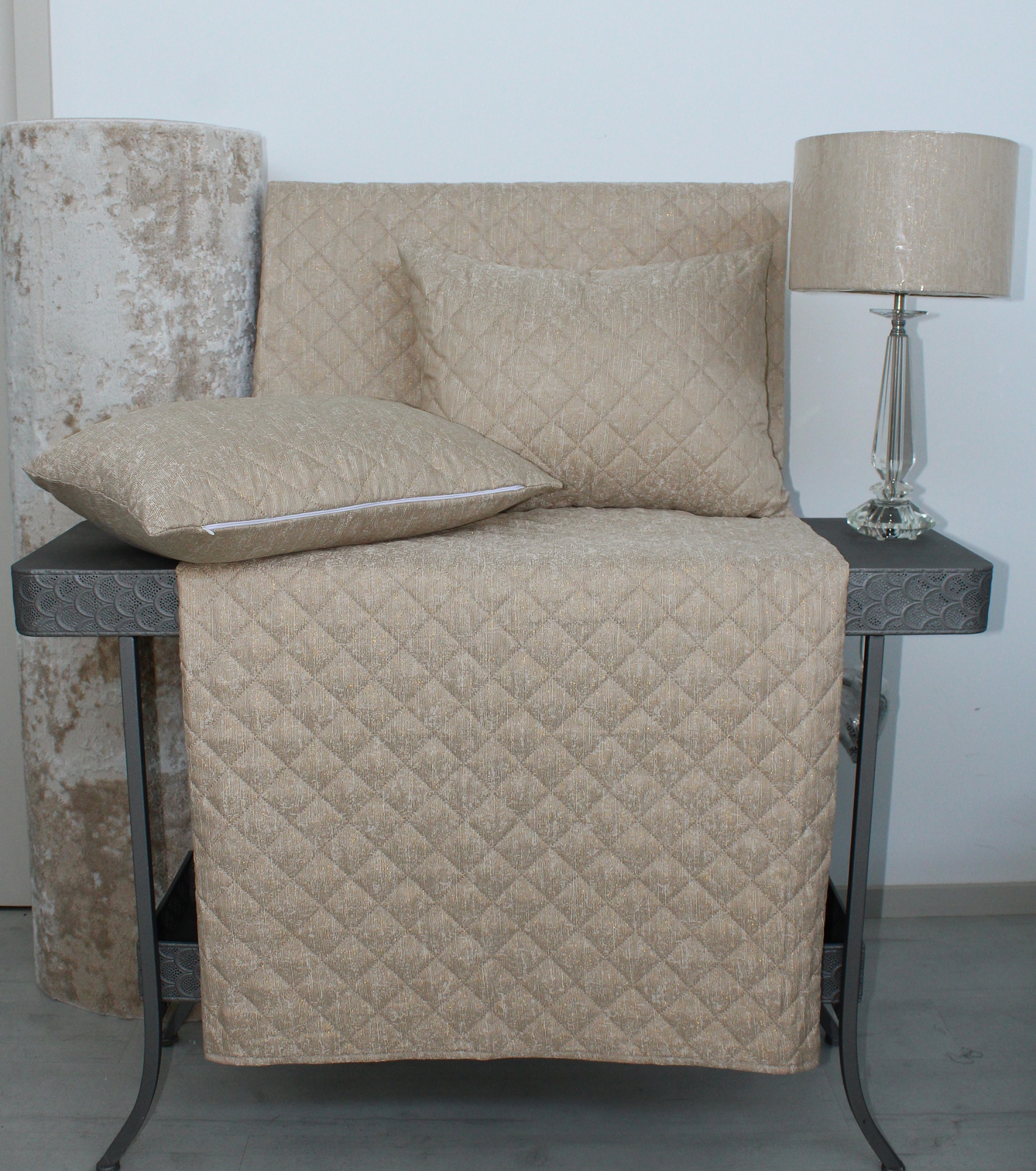 Tapete e almofadas bege acolchoadas com padrão de losangos sobre mesa preta com lâmpada