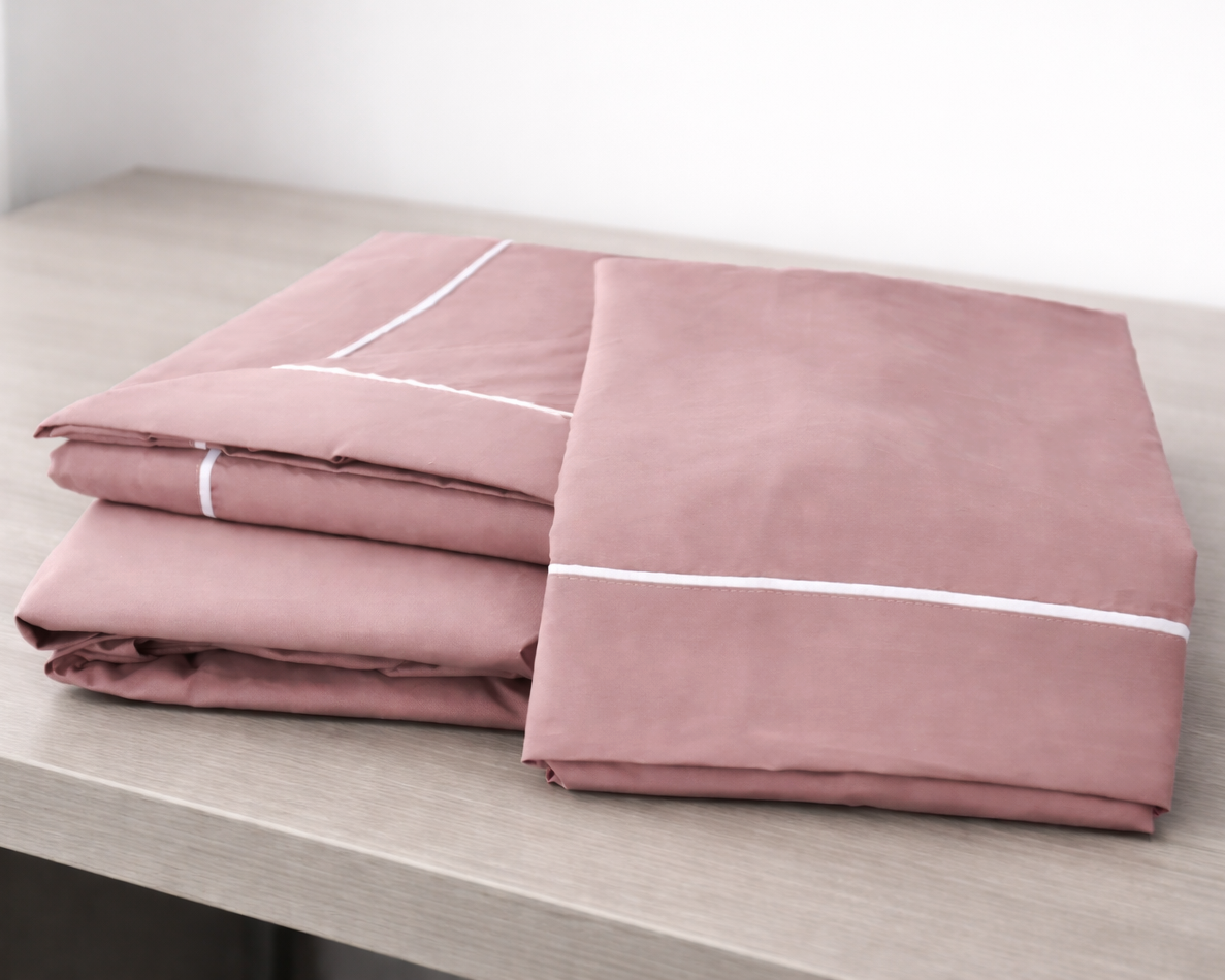 Conjunto de roupa de cama rosa salmão com linhas brancas dobrado sobre mesa