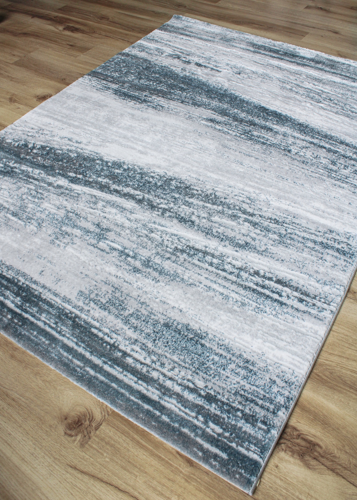 Tapete cinzento e branco com padrão abstrato sobre pavimento de madeira