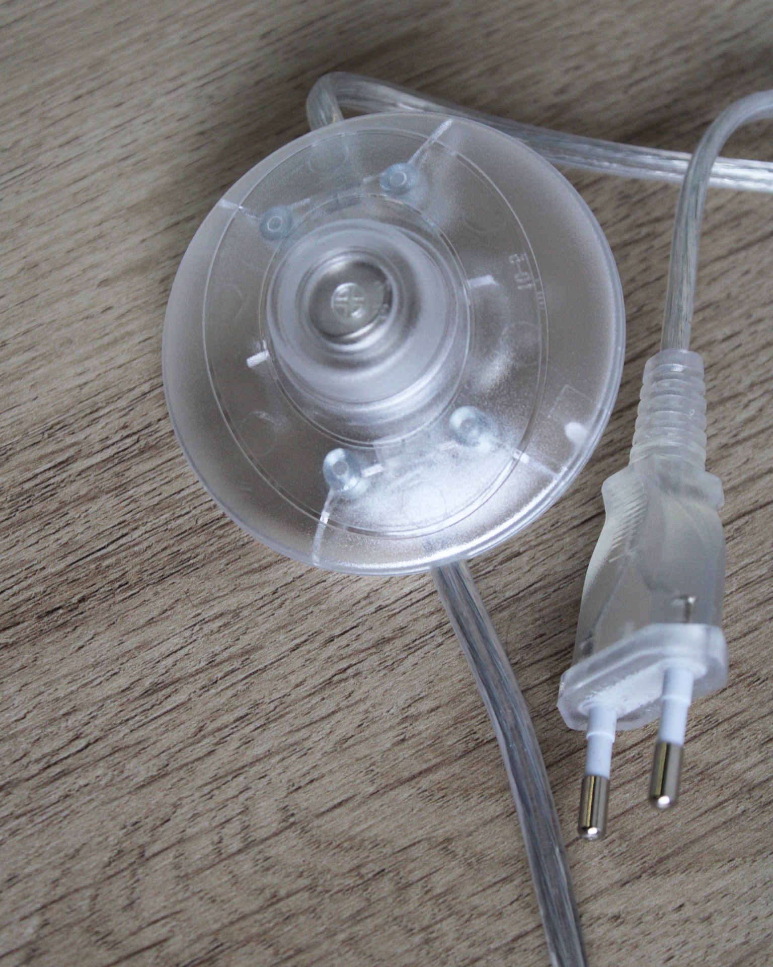 Cabo elétrico translúcido com interruptor redondo e ficha de dois pinos sobre madeira clara