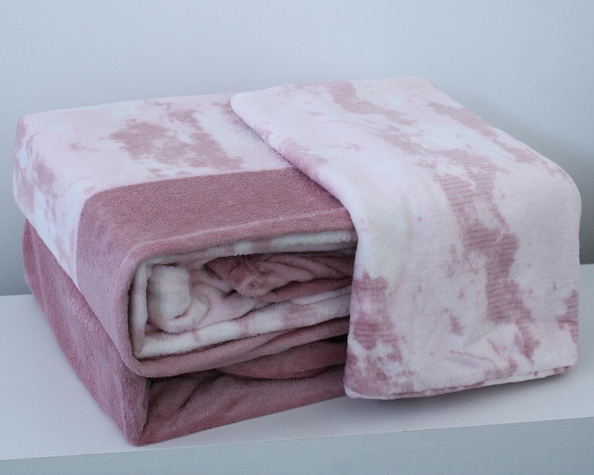 Manta felpuda rosa e branca dobrada numa superfície branca