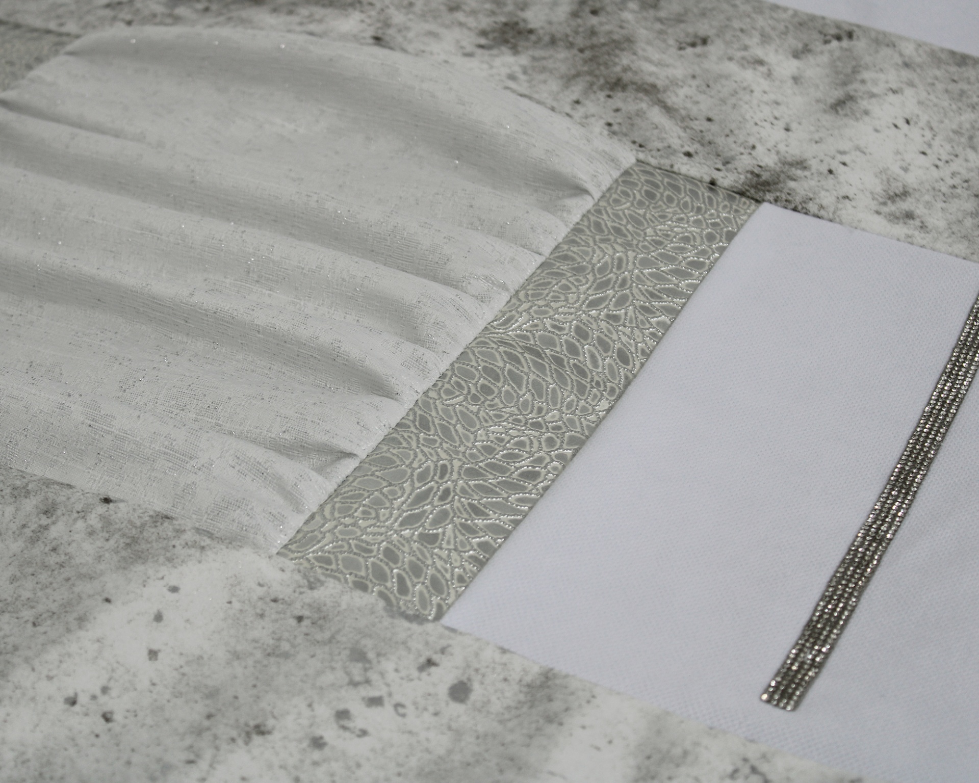 Capa de almofada cinza claro e branca com detalhes texturizados e faixa prateada