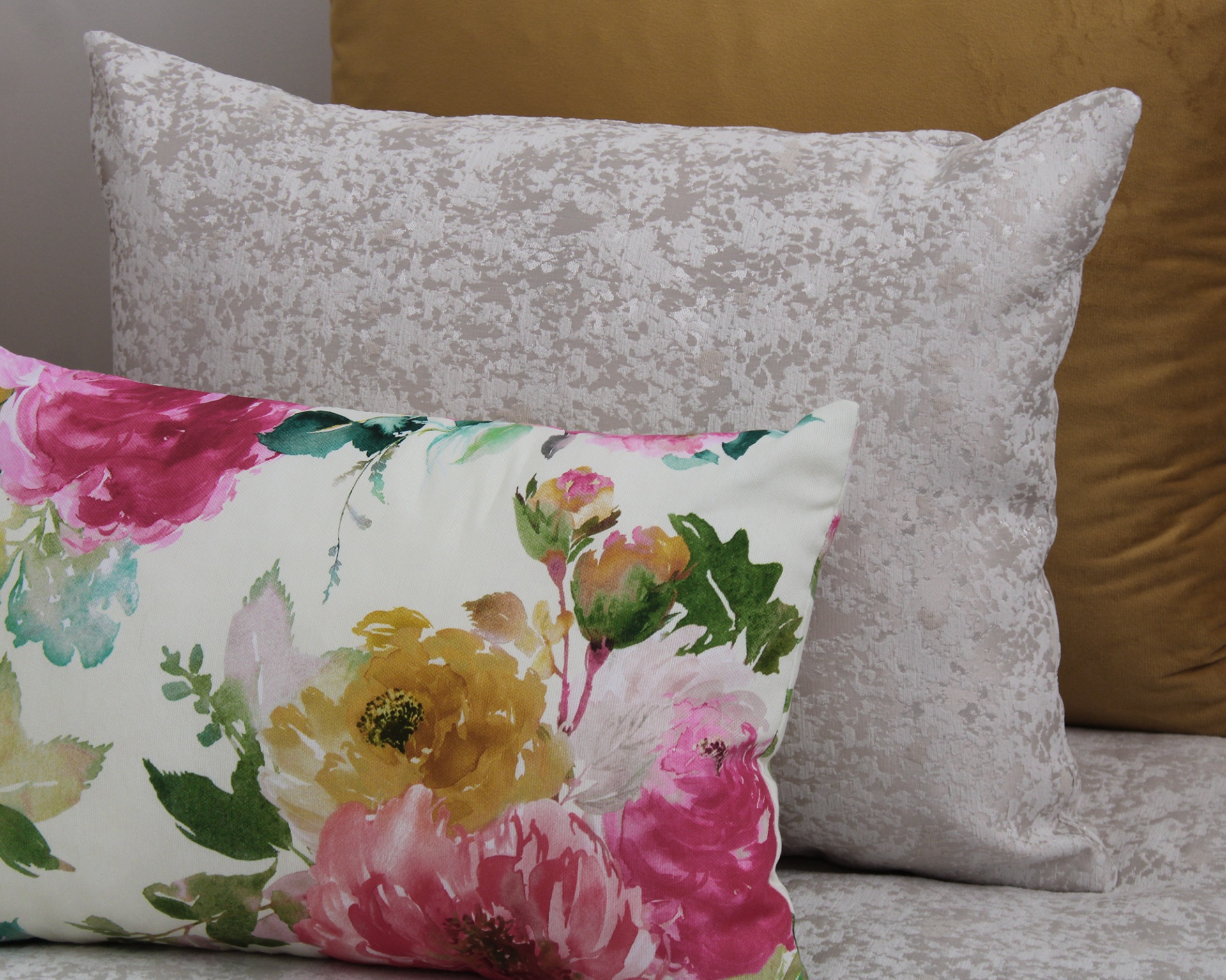Três almofadas decorativas com padrões florais, textura abstrata e cor lisa mostarda.
