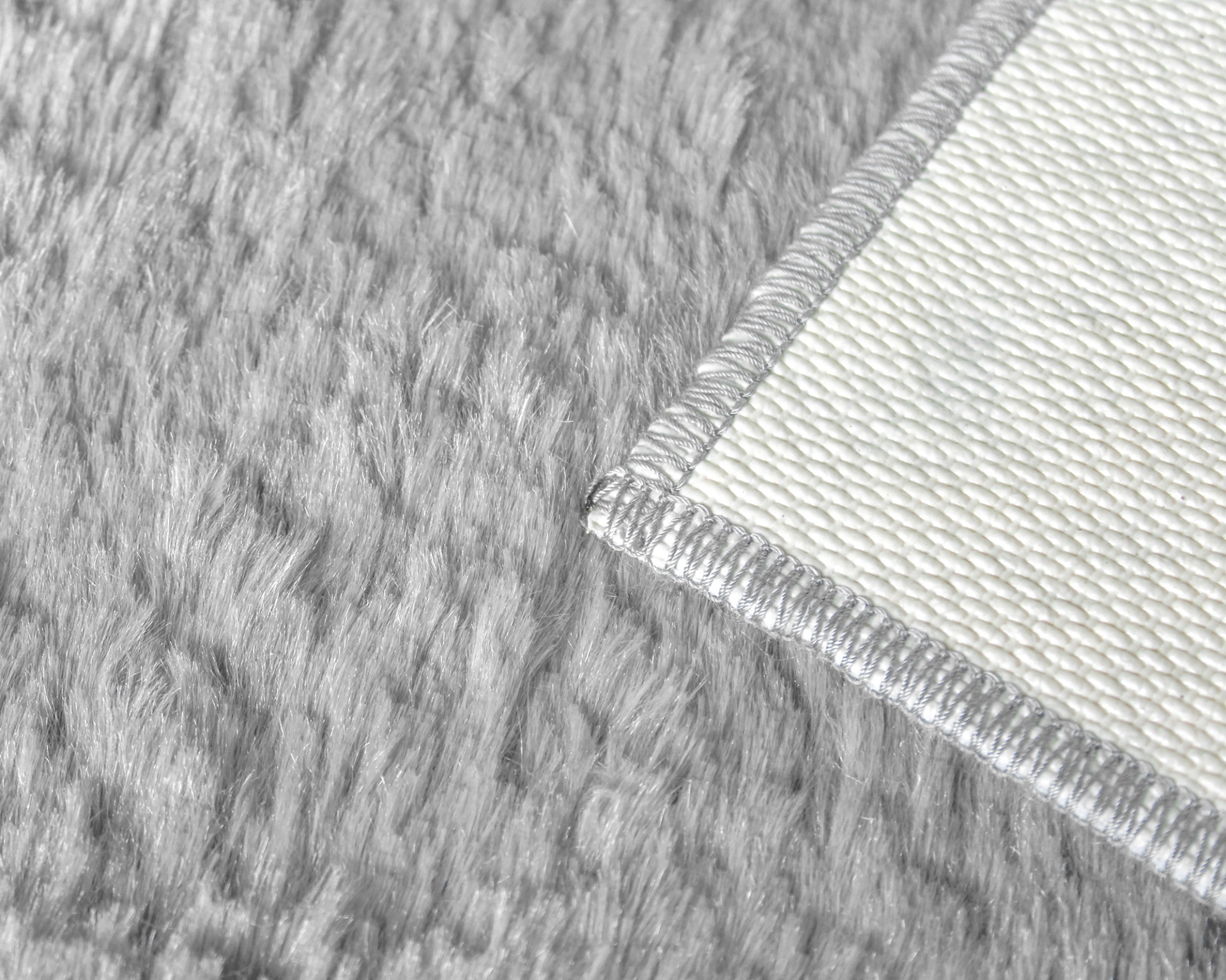 Pormenor de tapete cinzento com pelo e tapete branco com borda costurada