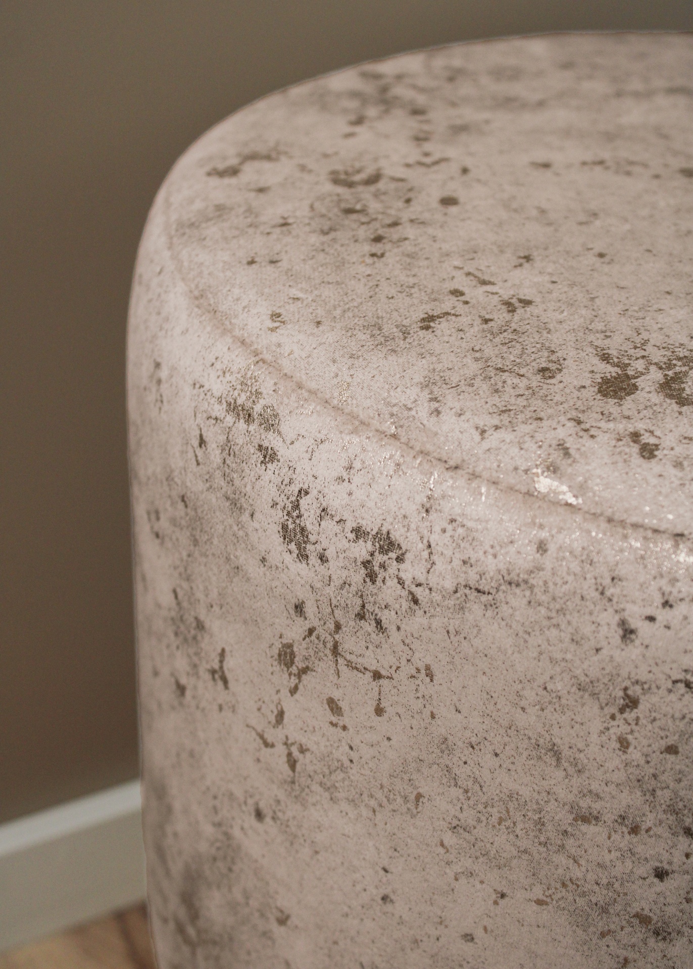 Pufe cilíndrico em tecido aveludado bege com manchas castanhas, em ambiente interior