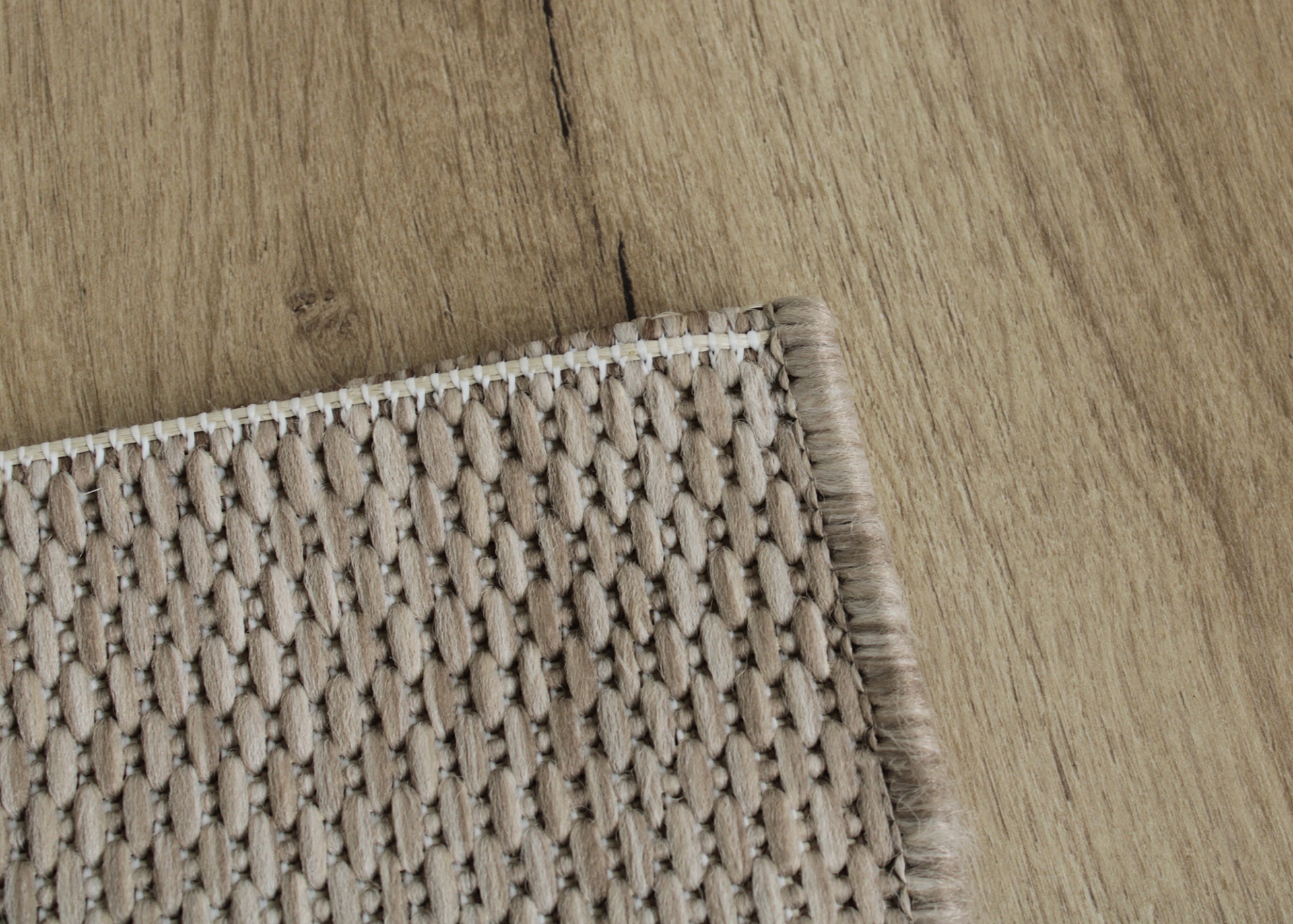 Tapete bege trançado com franja sobre chão de madeira clara