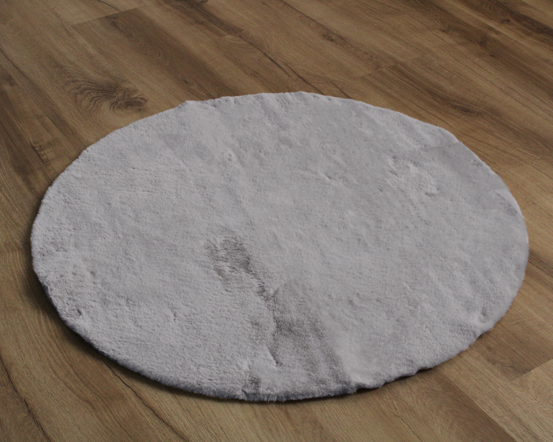 Tapete redondo branco com manchas sobre chão de madeira clara