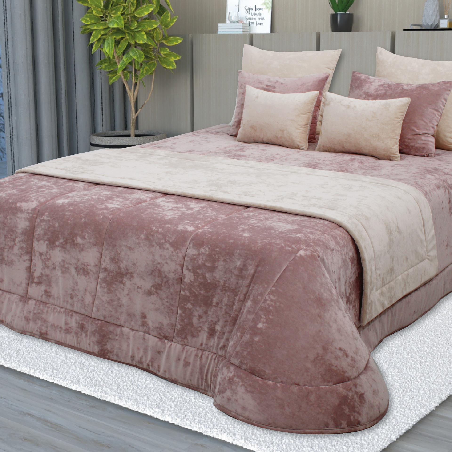 Jogo de cama rosa claro e bege aveludado numa cama com almofadas, tapete branco e chão de madeira.