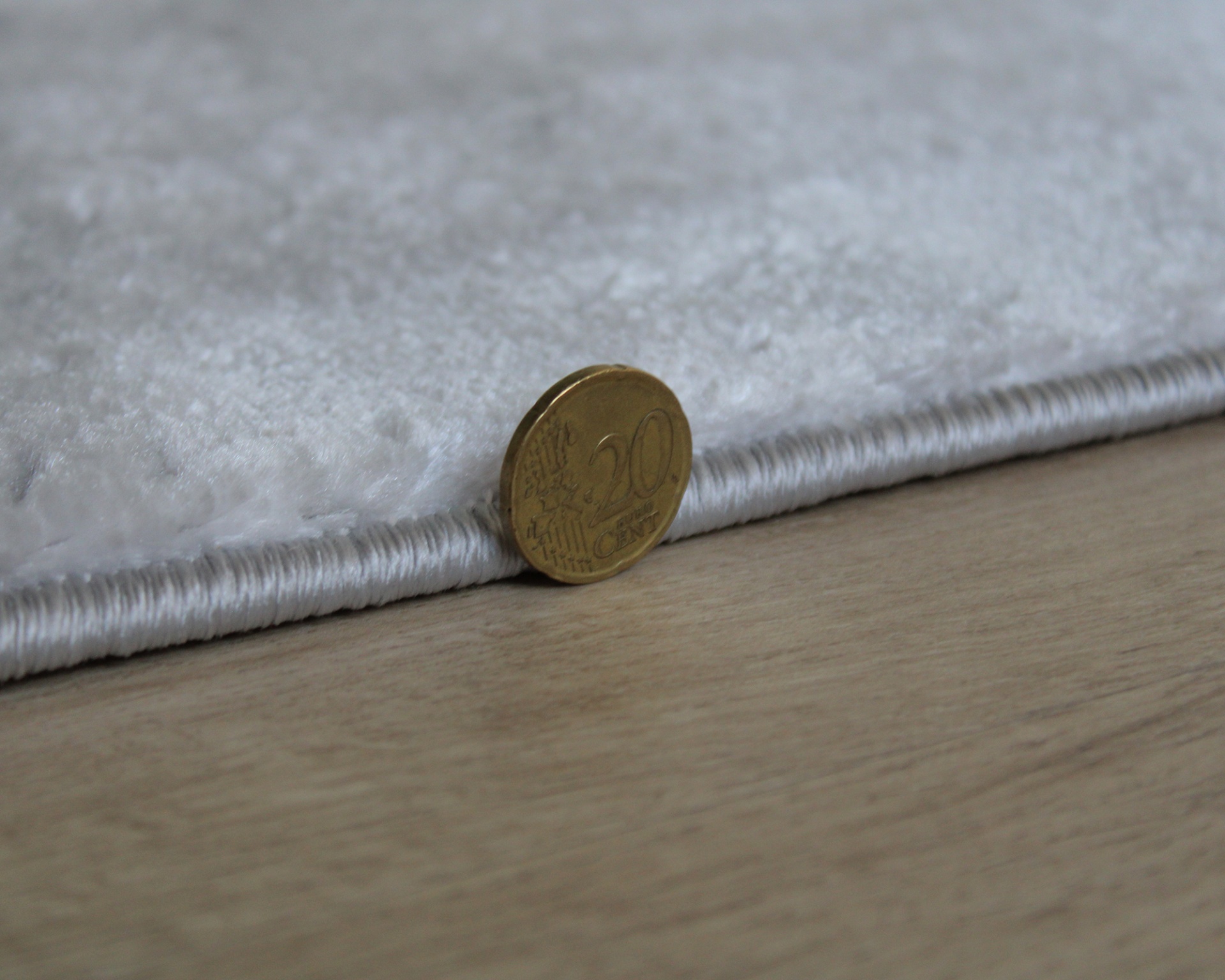 Tapete branco macio com borda branca e moeda de 20 cêntimos encostada para referência da espessura