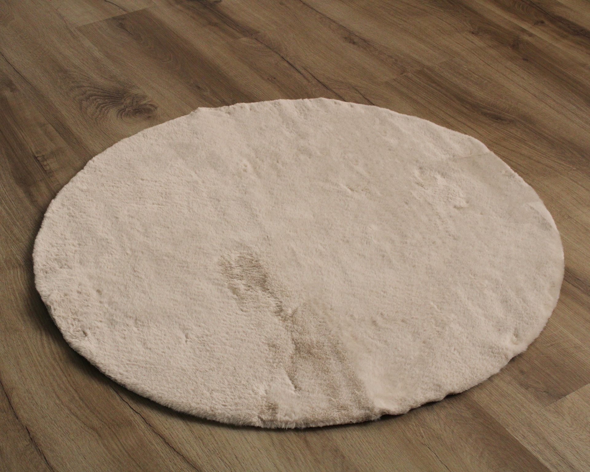 Tapete redondo bege claro com mancha em chão de madeira