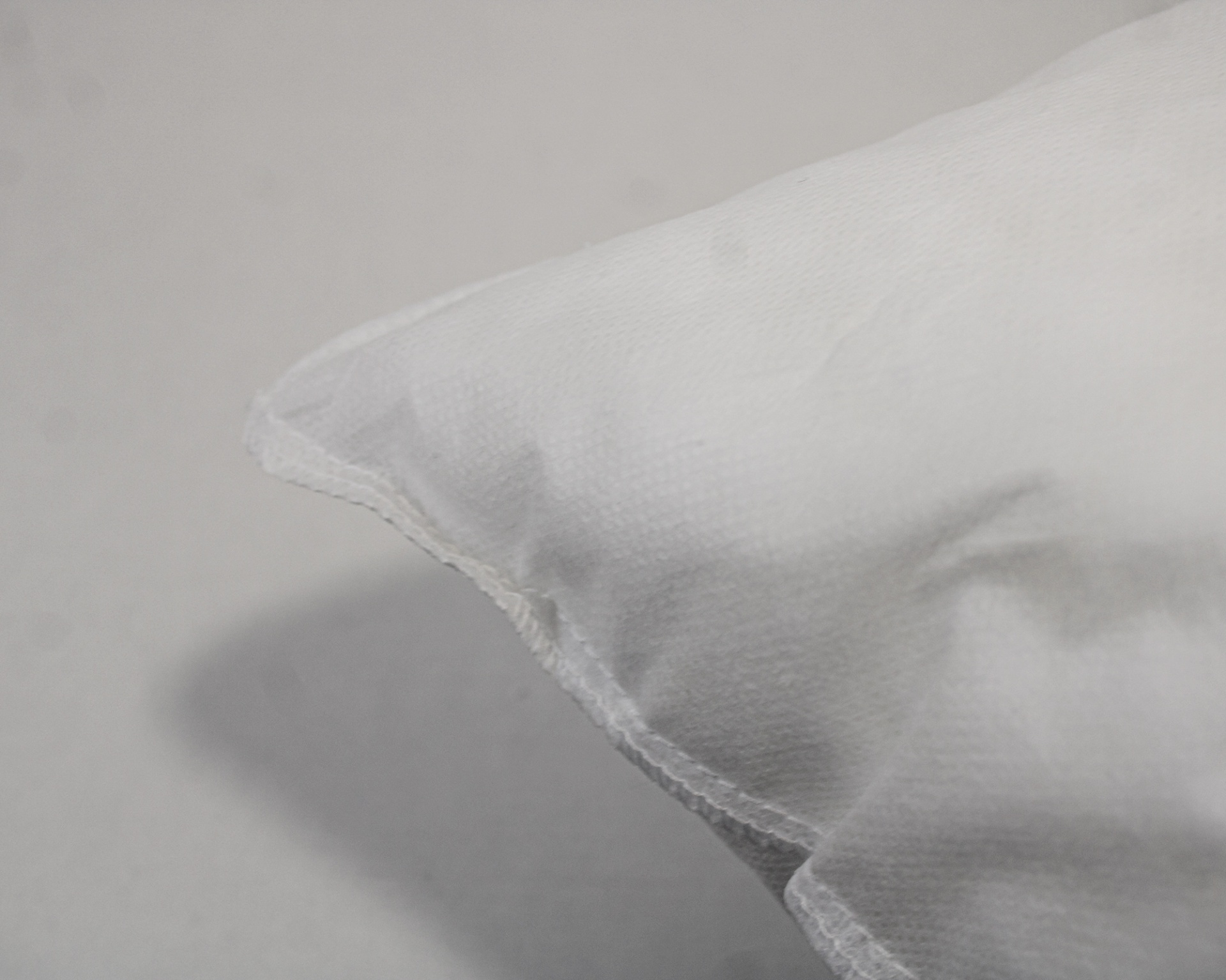 Canto de almofada branca com costura visível sobre superfície cinzenta