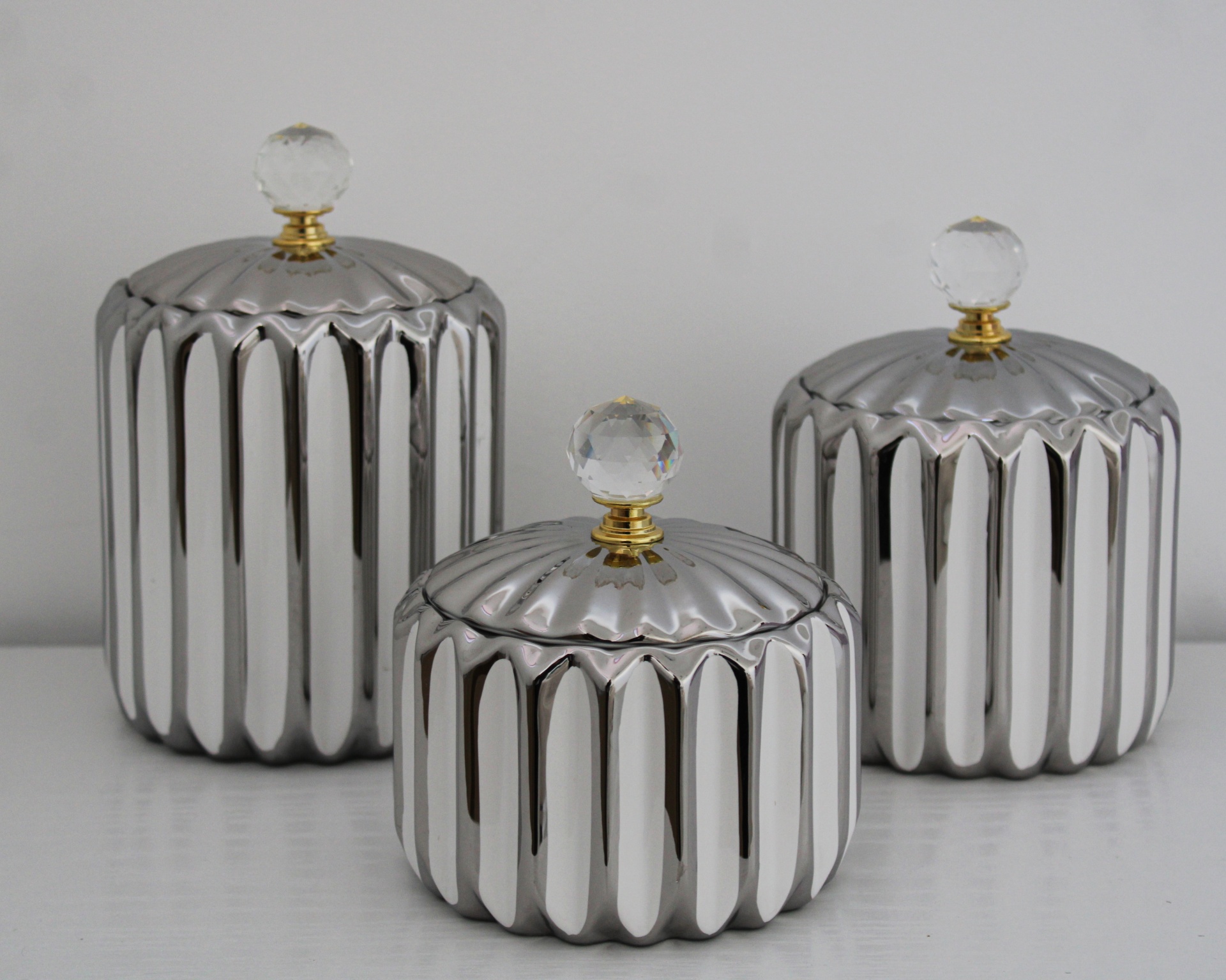 Três frascos metálicos prateados com tampas e puxadores de bola transparente