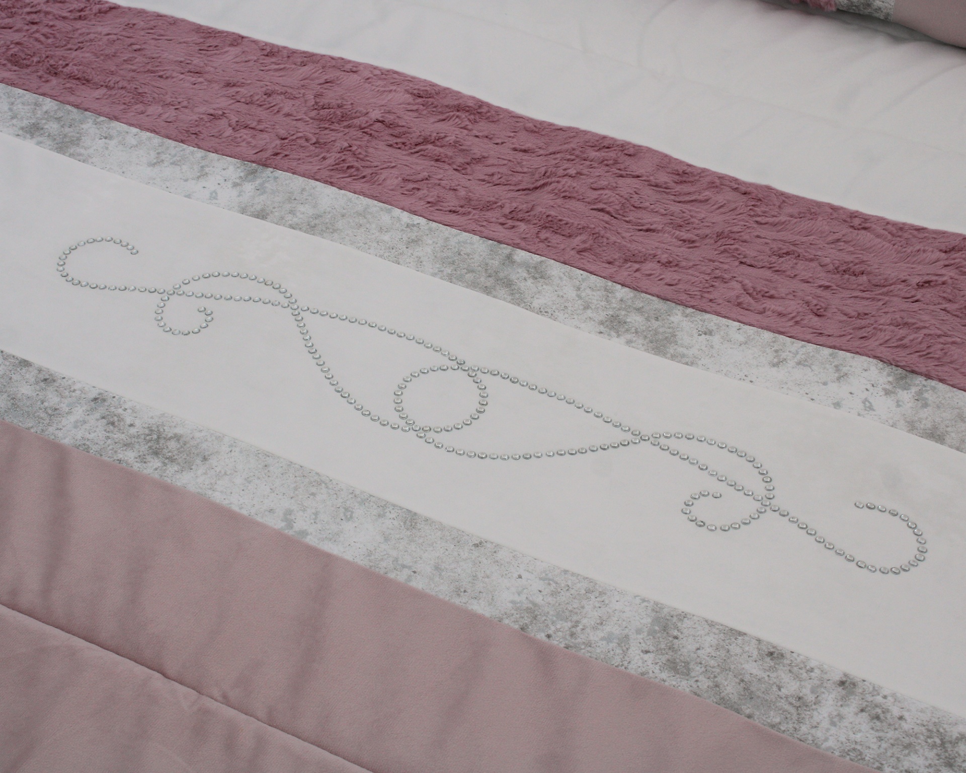 Detalhe de têxtil de cama rosa, branco e cinza com padrões e texturas variadas