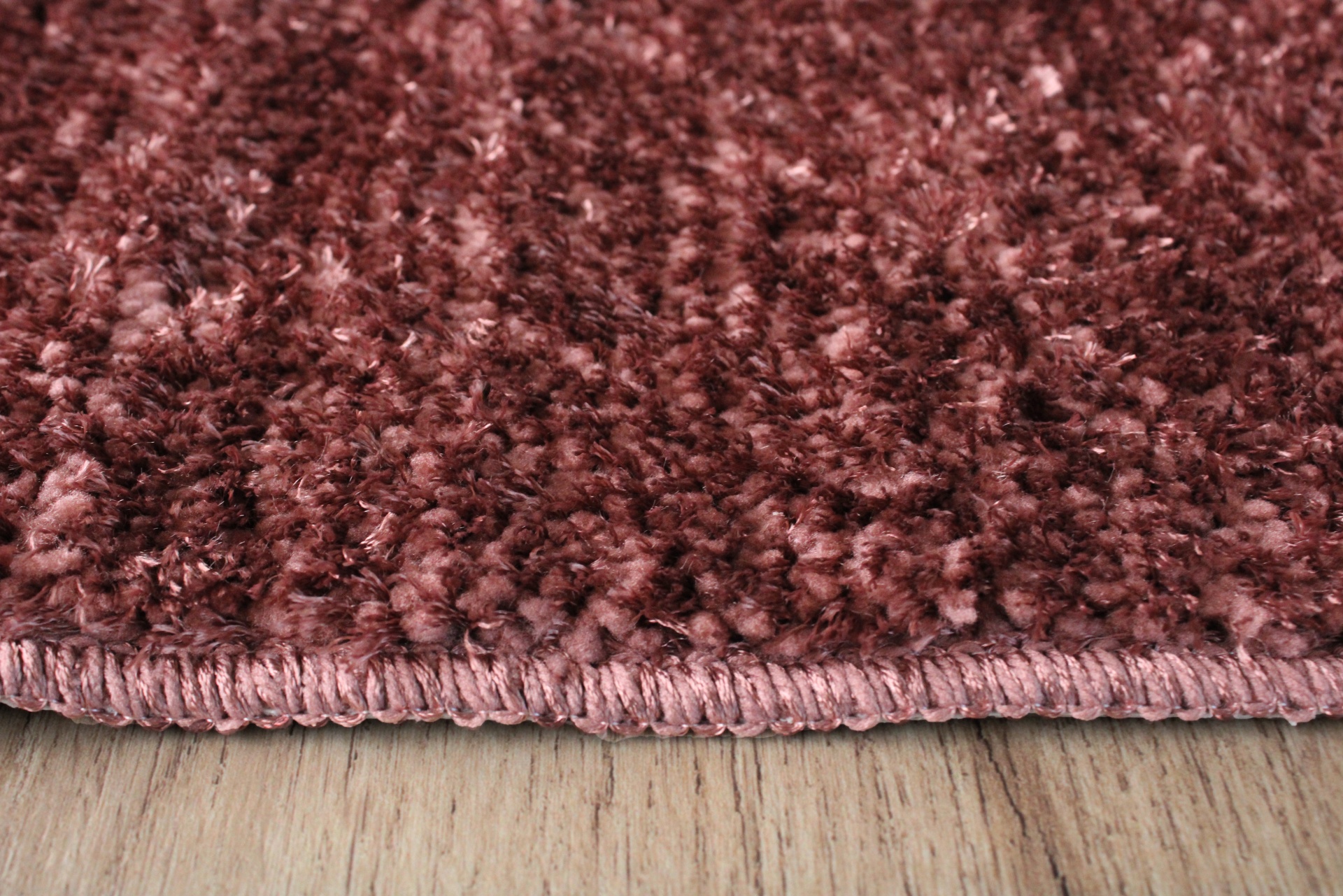 Tapete felpudo bordô com acabamento costurado sobre chão de madeira clara