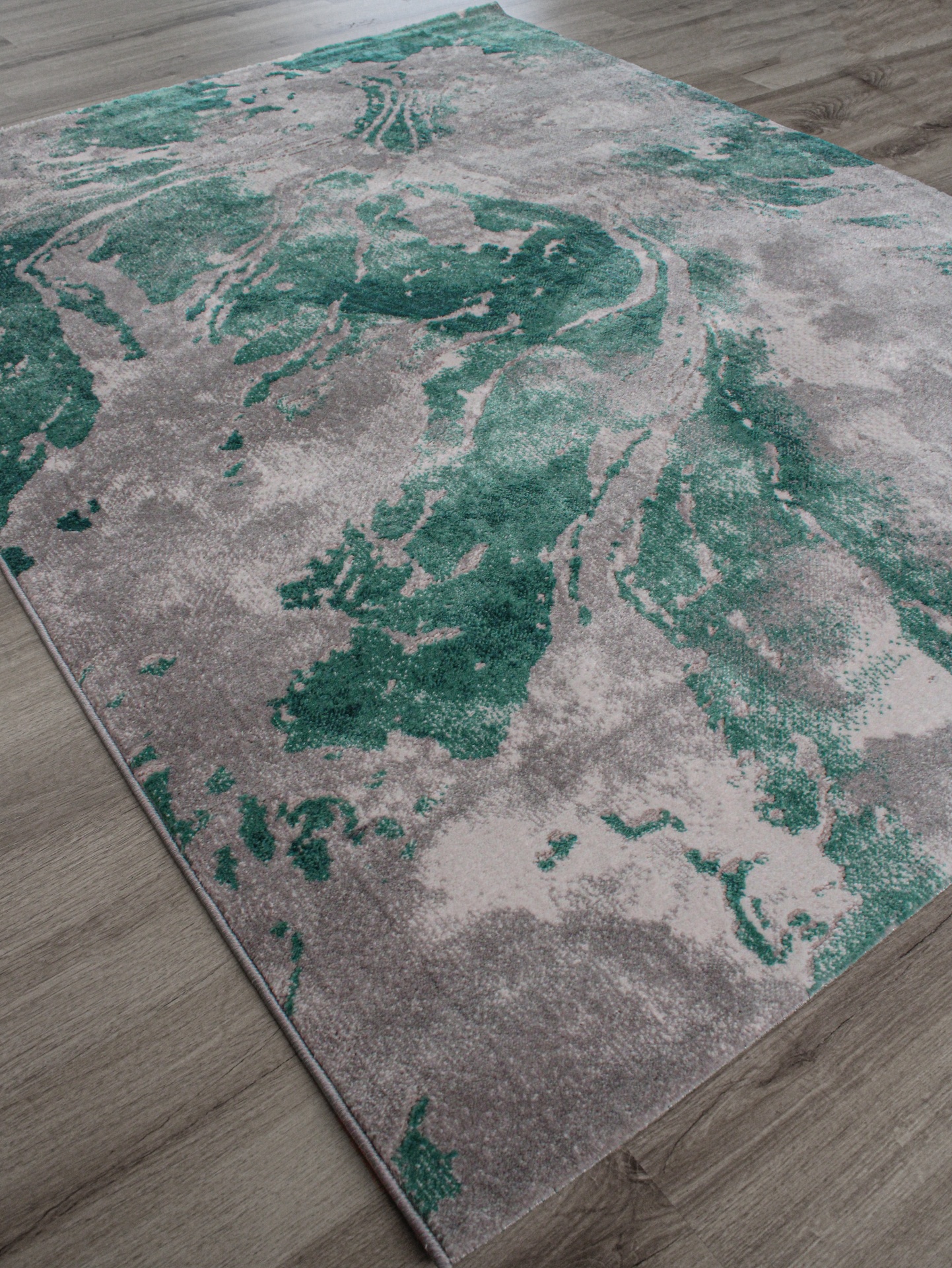 Tapete decorativo cinza e verde-água com padrão abstrato sobre chão de madeira