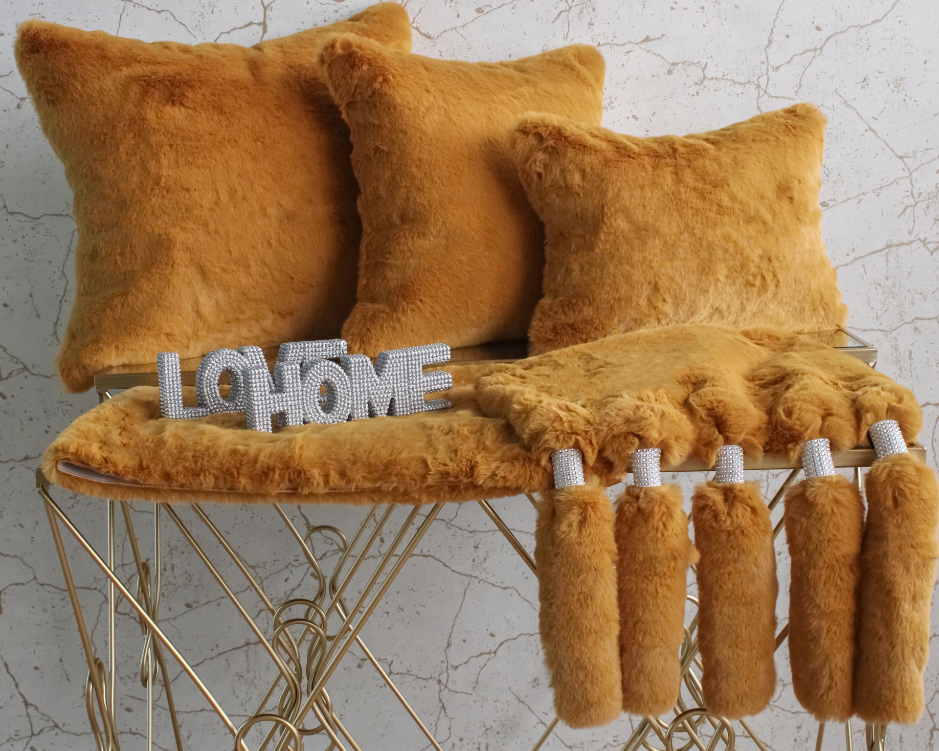 Almofadas e manta castanhas mostarda felpudas sobre banco dourado com placa LOHOME