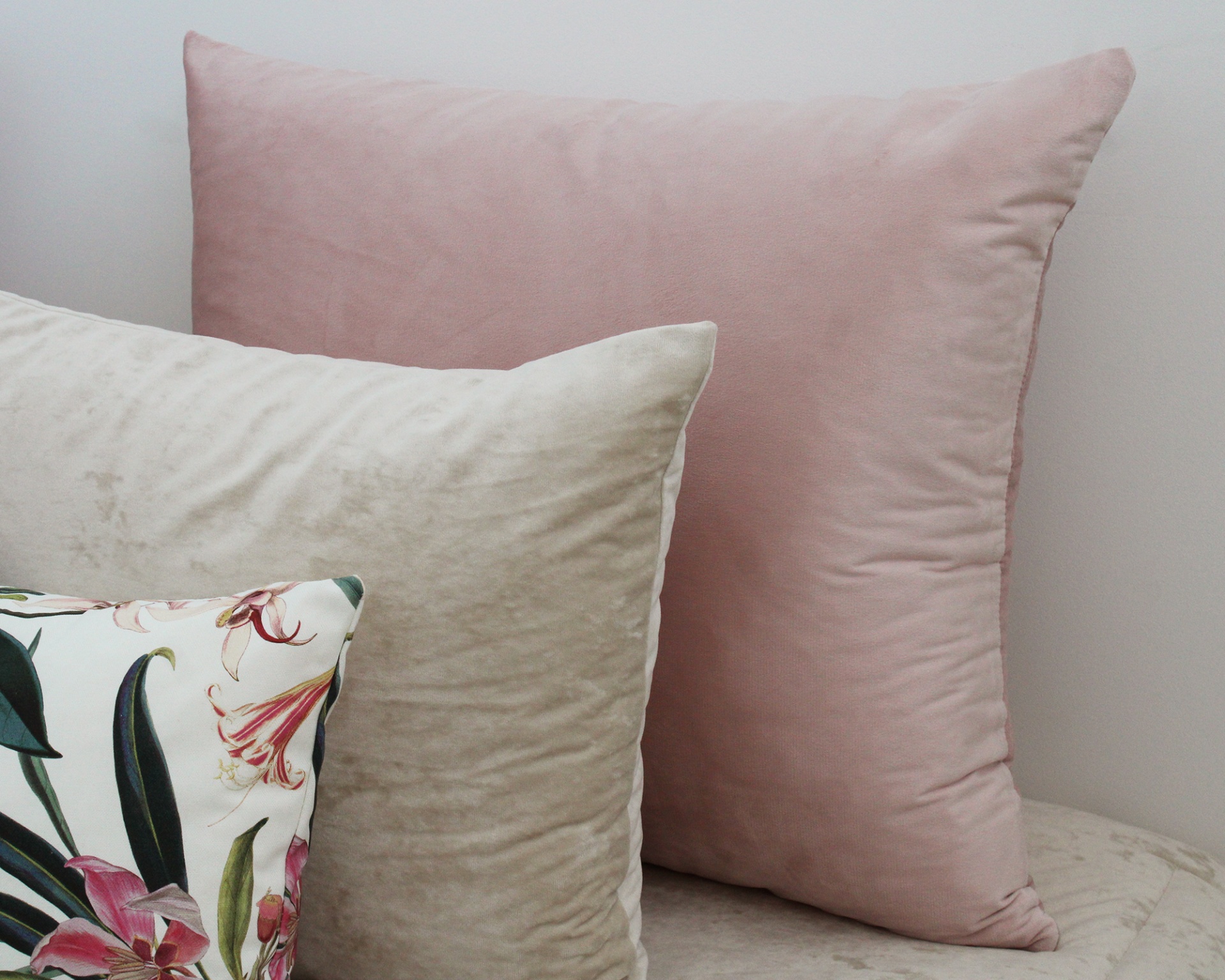 Três almofadas aveludadas e com padrão floral em sofá claro.