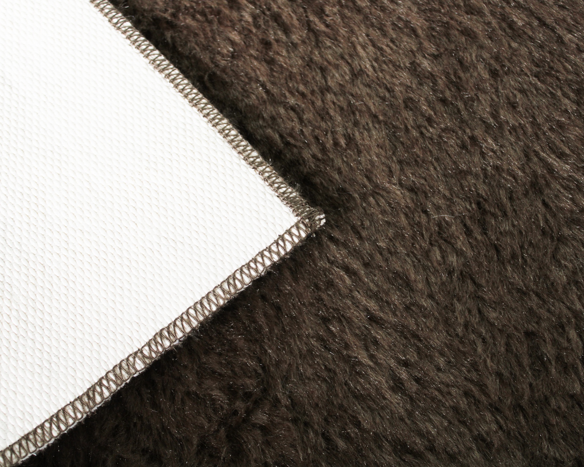 Canto de tapete branco com costura marrom sobre superfície peluda castanha