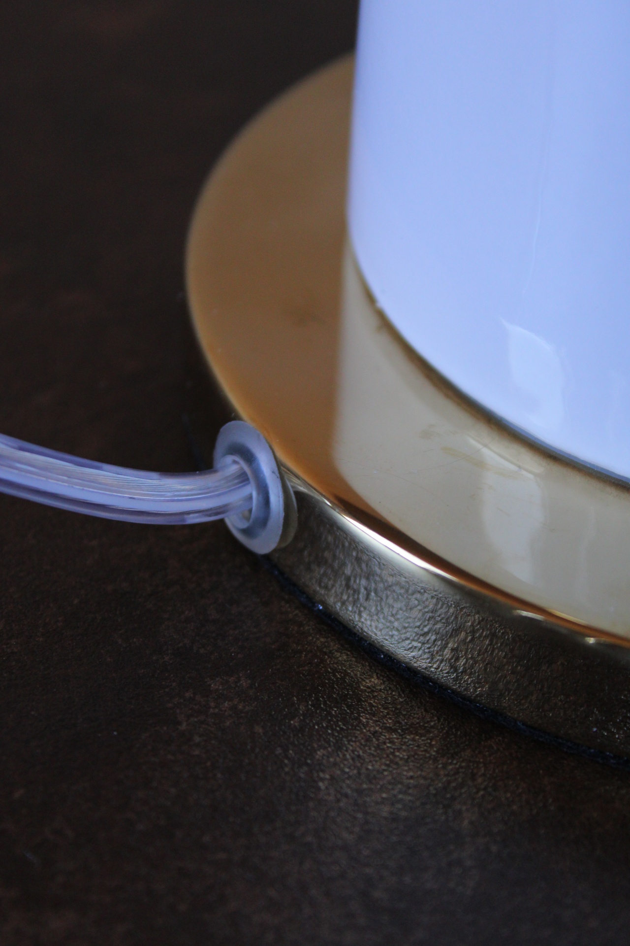 Base dourada de objeto branco com cabo transparente numa superfície preta.